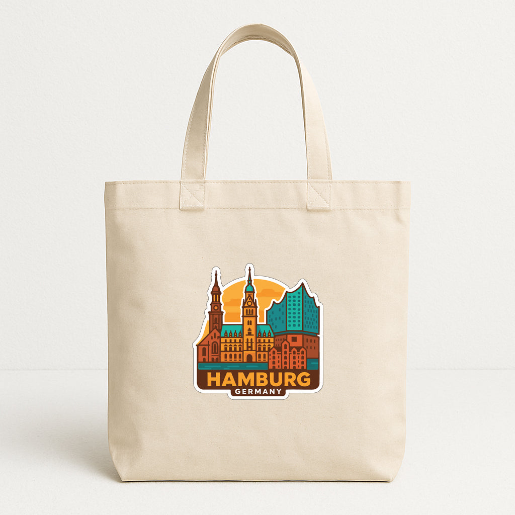 A beige tote bag with a sticker depicting the skyline of Hamburg, Germany.