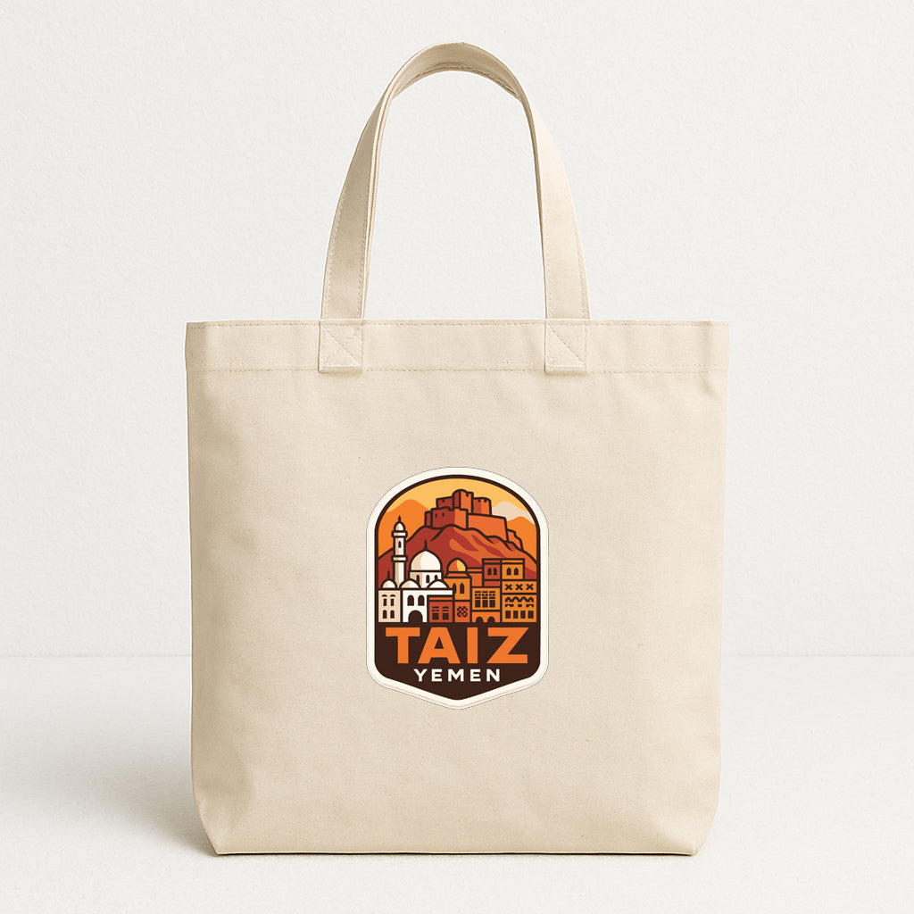 A beige tote bag with a graphic design featuring a cityscape and the text "TAIZ YEMEN" printed on it.