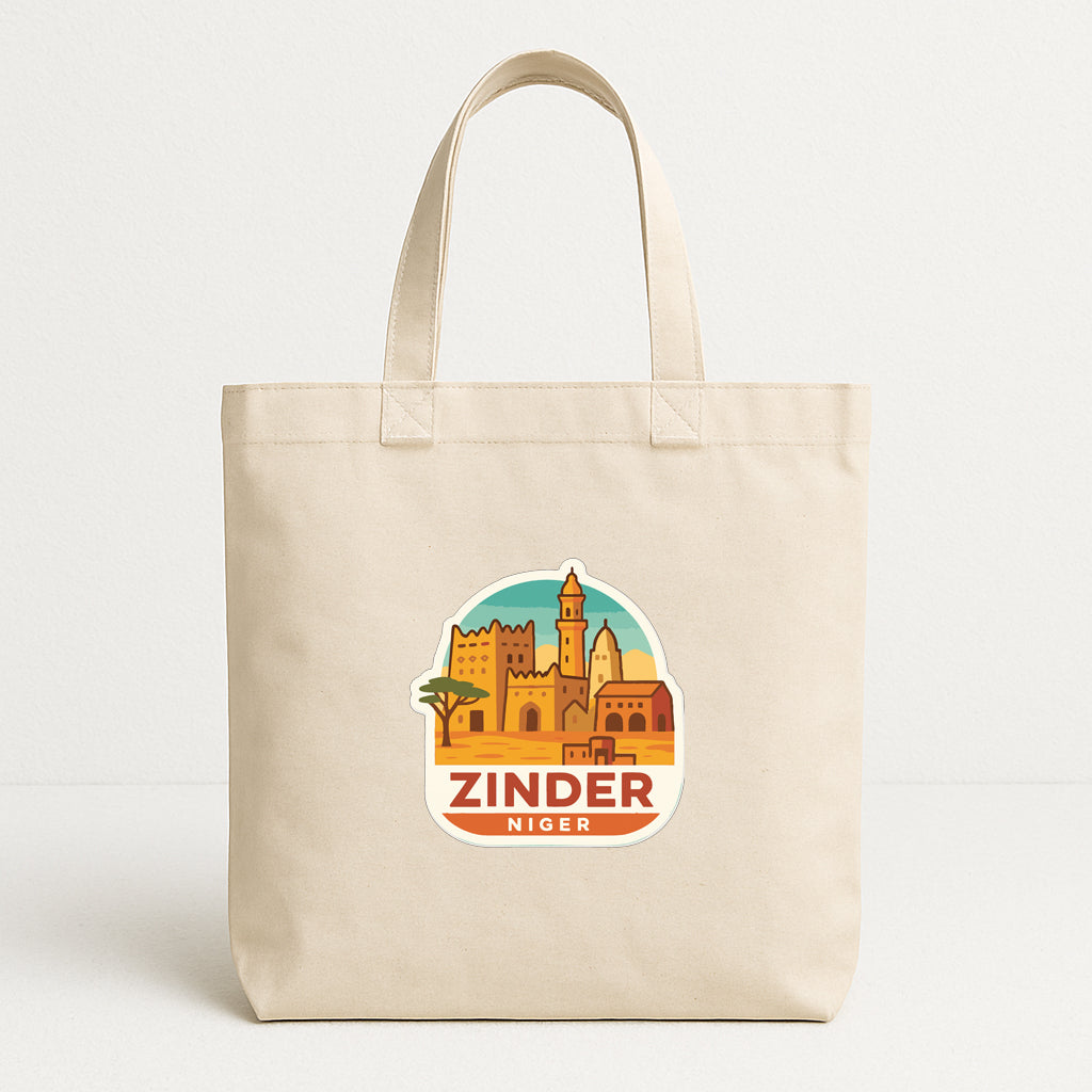 A beige tote bag with a printed sticker depicting a cityscape and the text "ZINDER NIGER" printed on it.