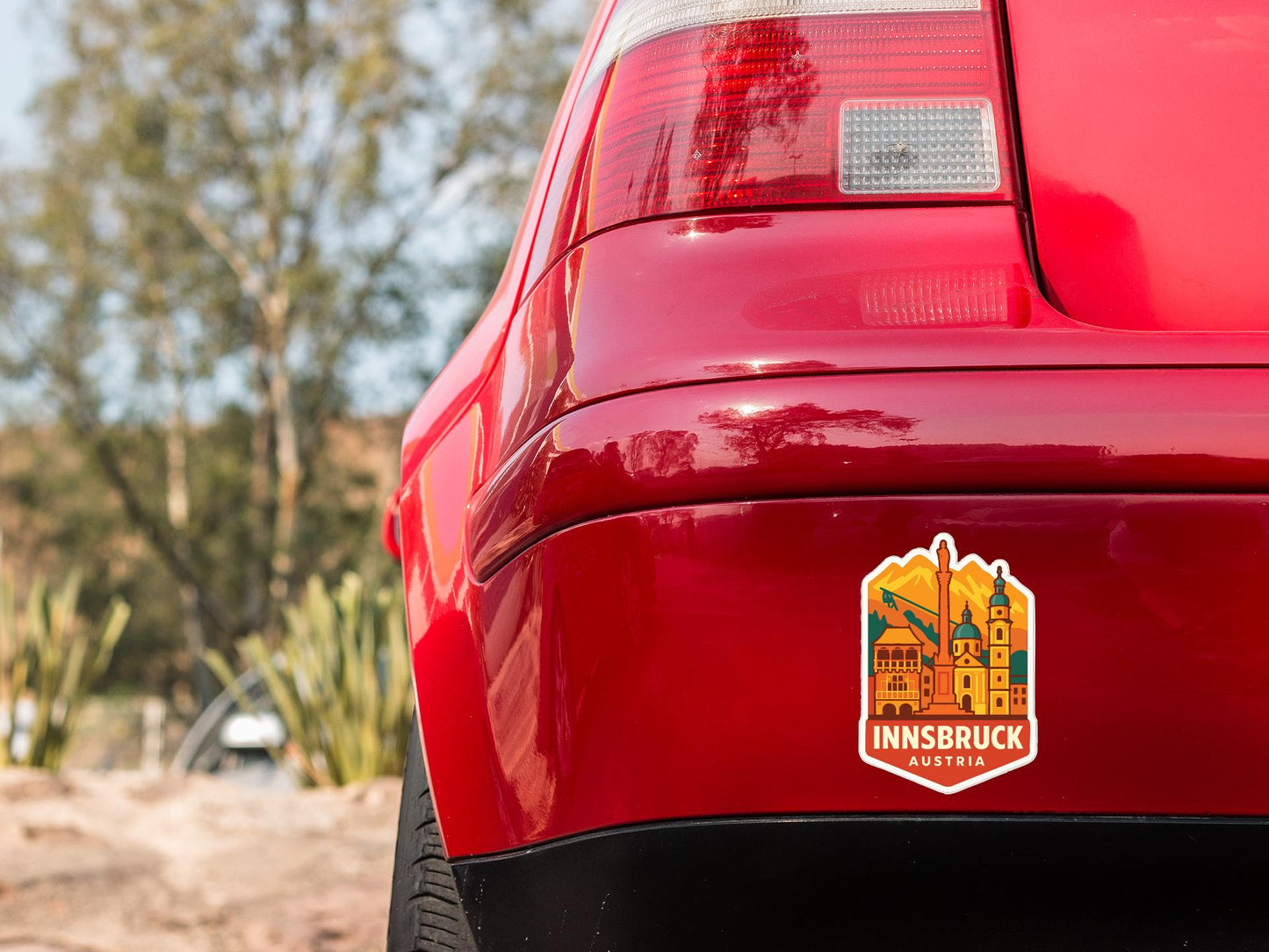 the rear end of a red car with a sticker on the trunk that says "INSBRUCK AUSTRIA".