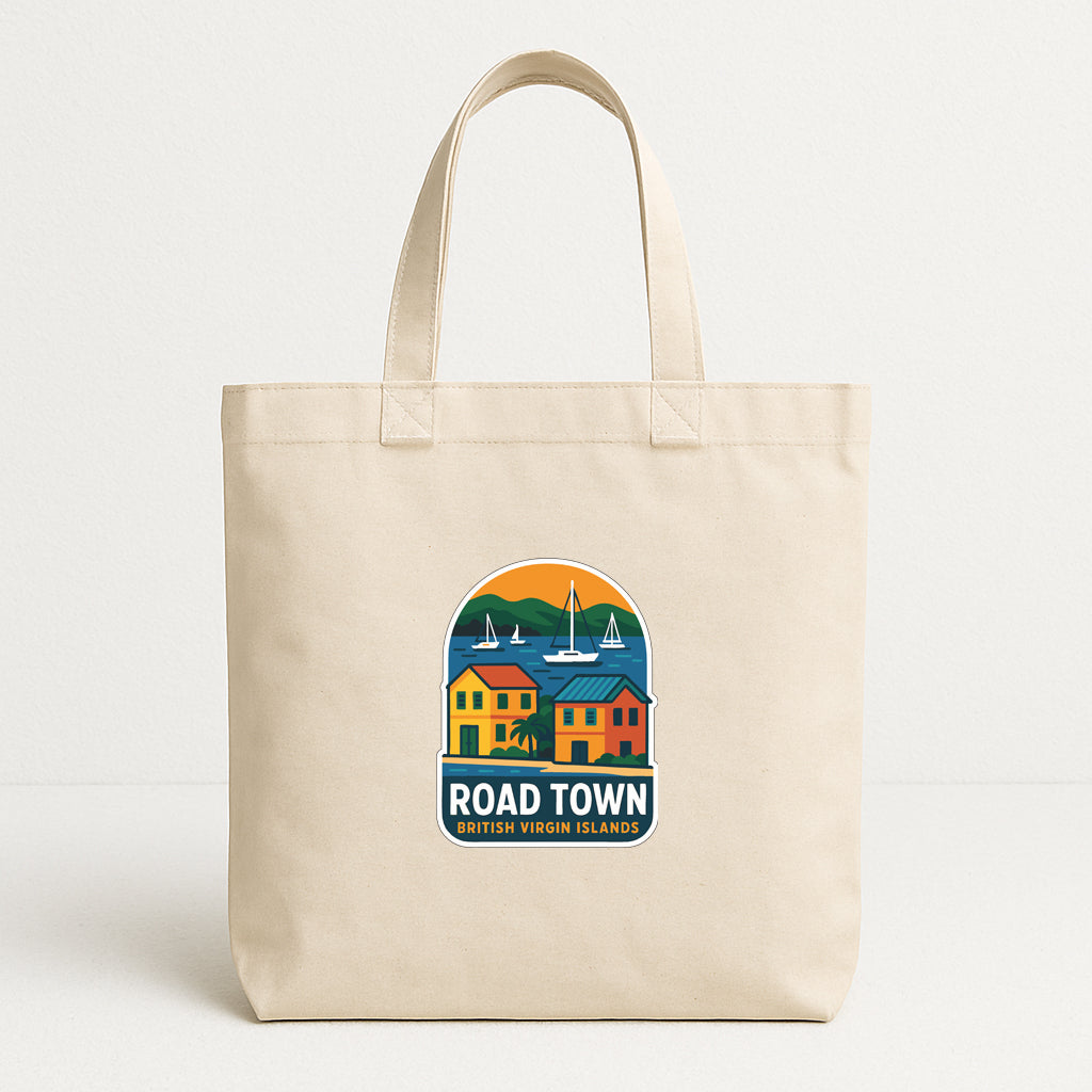 A beige tote bag with a colorful graphic design depicting a coastal town scene, including houses, boats, and mountains.