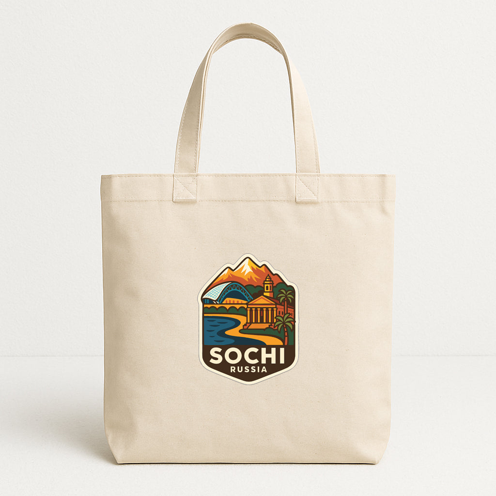 A beige tote bag with a graphic design depicting a scenic landscape with mountains, buildings, and a body of water.
