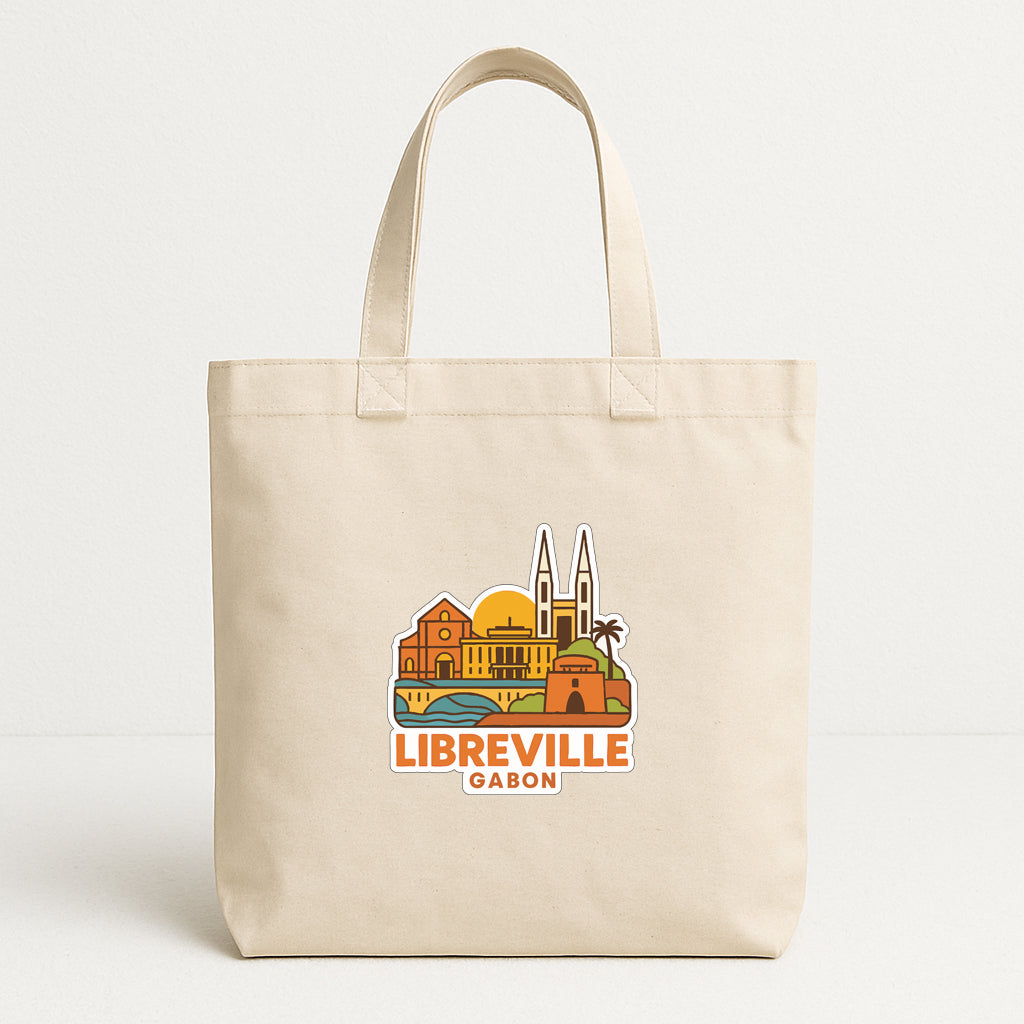A beige tote bag with a graphic design depicting the city of Libreville, Gabon, featuring landmarks and a sun.