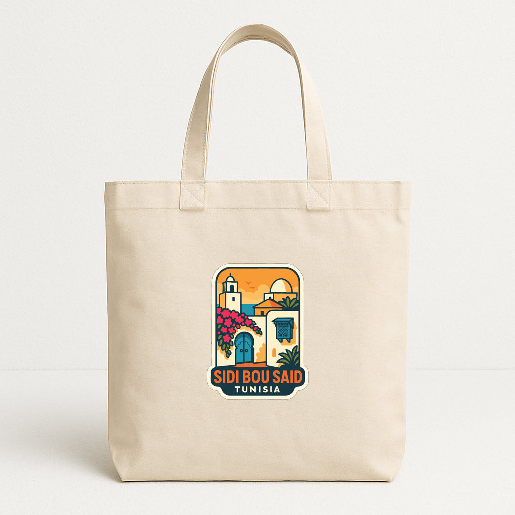 A beige tote bag with a graphic design featuring a colorful illustration of a cityscape and the text "SIDI BOU SAID TUNISIA".