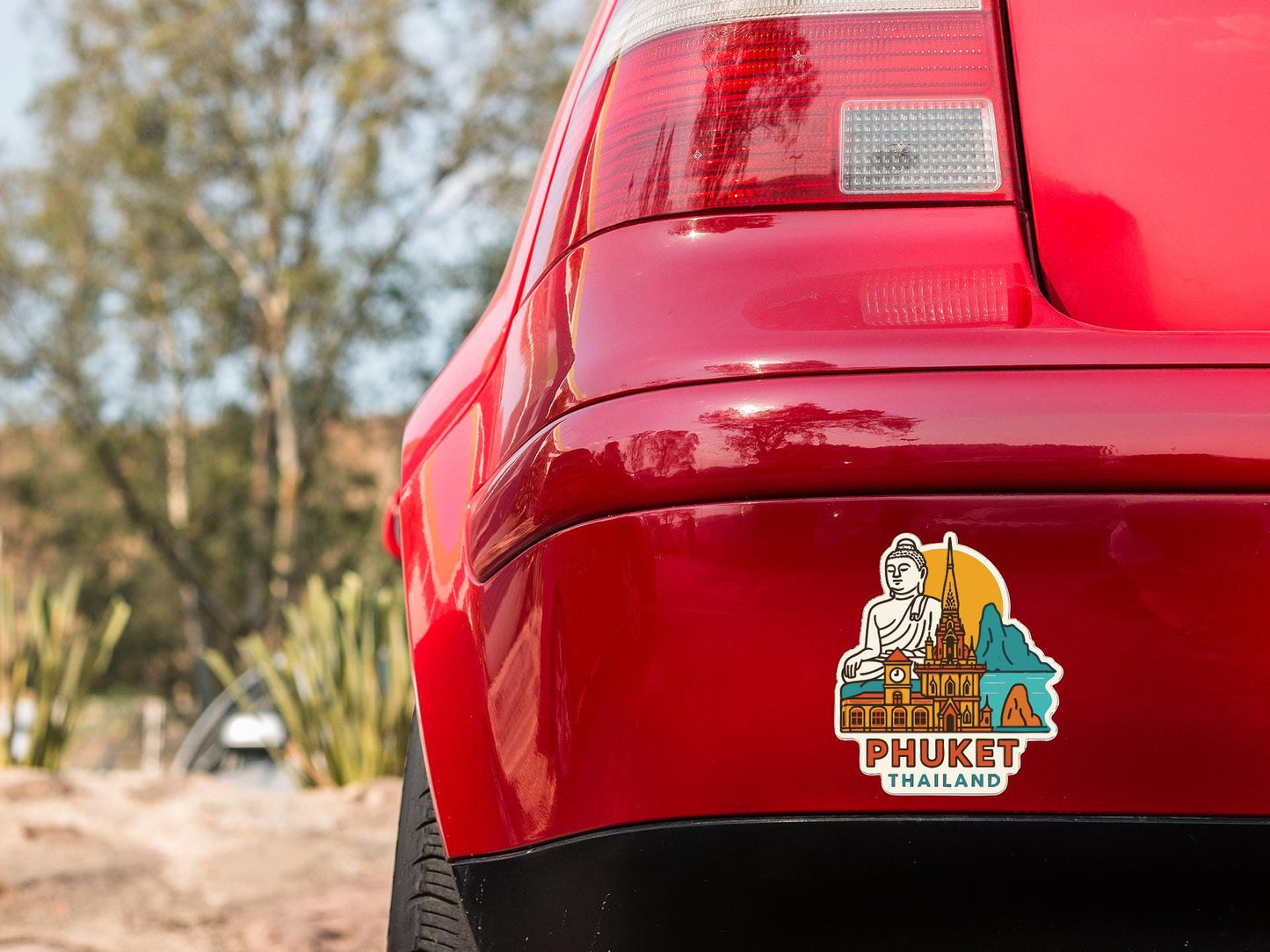 the rear end of a red car with a sticker on it, featuring a Buddha statue and a tropical landscape.