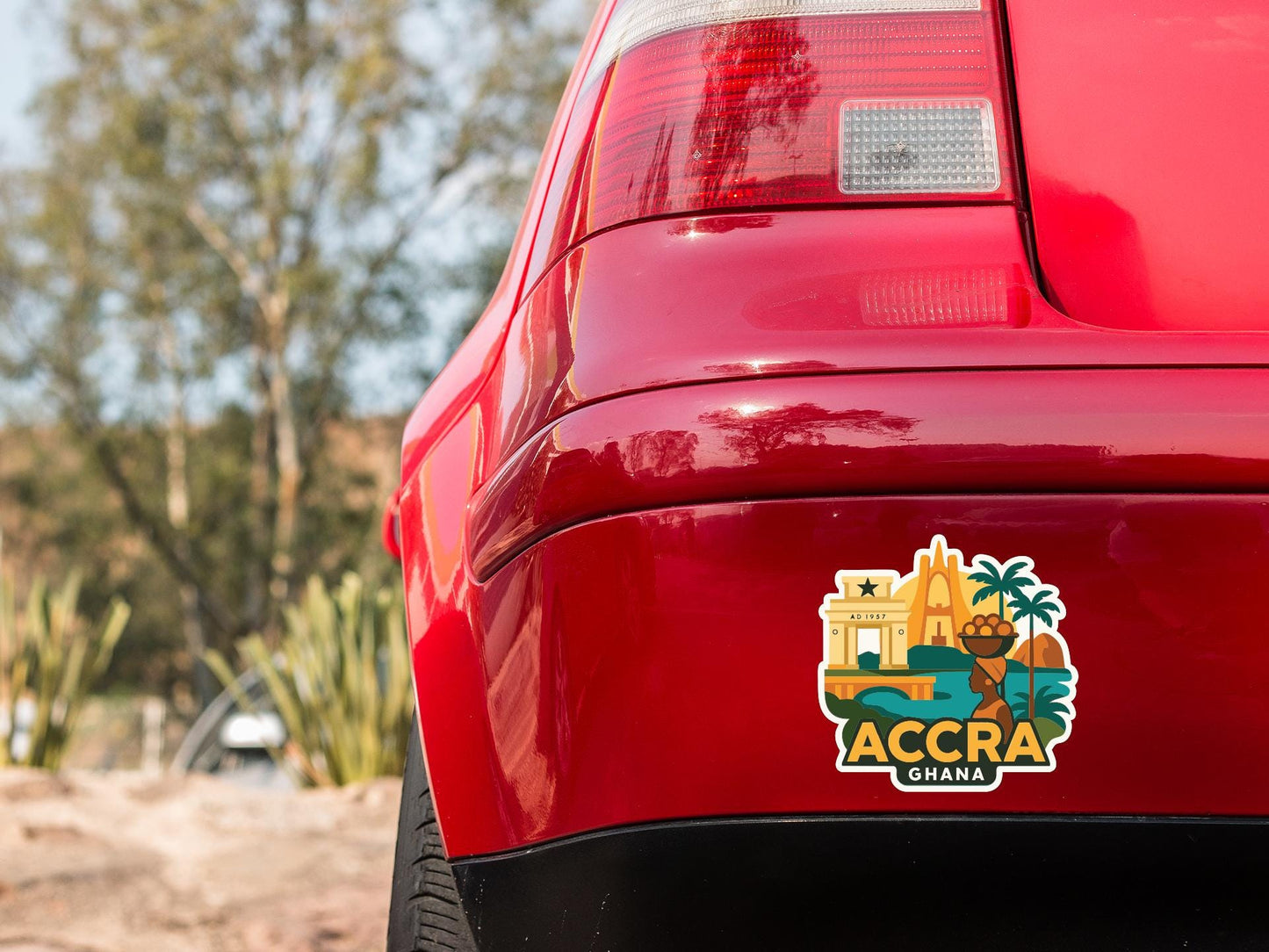 the rear end of a red car with a sticker on the trunk that features an illustration of Accra, Ghana.