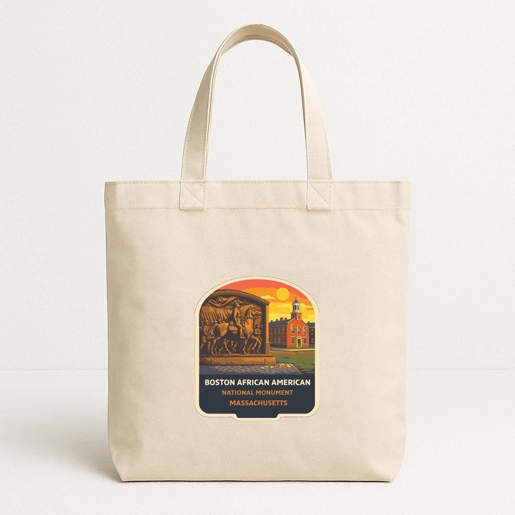 A beige tote bag with a printed design featuring a cityscape and a historical monument, along with the text "BOSTON AFRICAN AMERICAN NATIONAL MONUMENT MAESCHUSETTS".