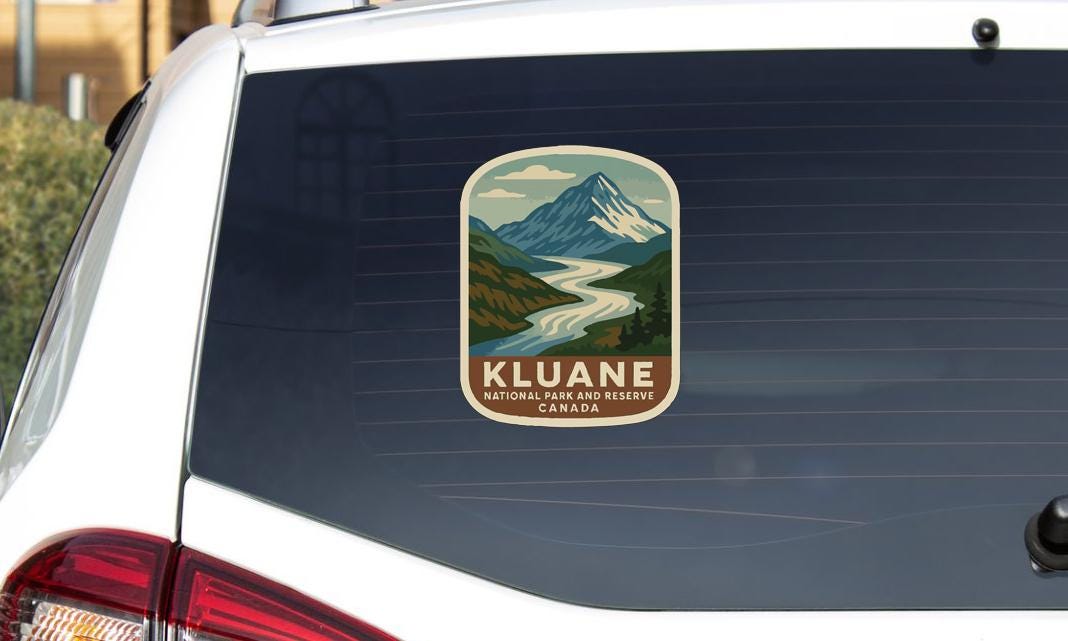 A sticker on the rear window of a vehicle, depicting a mountain landscape with a river.