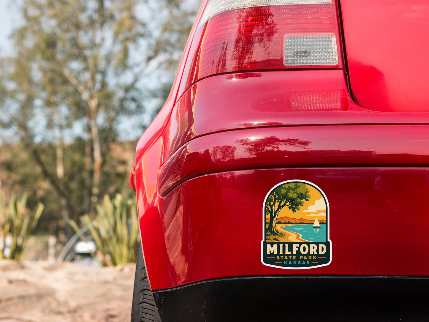 the rear end of a red car with a sticker on the bumper that says "Milford State Park Kansas".