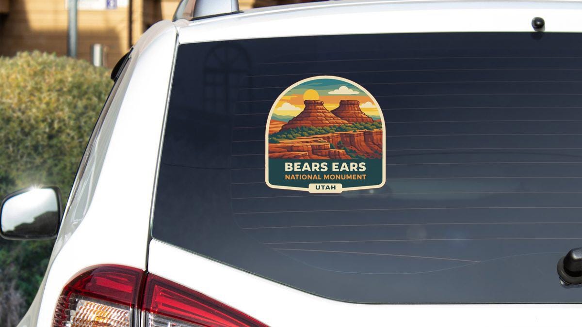 A sticker on the rear window of a white car, depicting a scenic landscape with mountains and a monument.