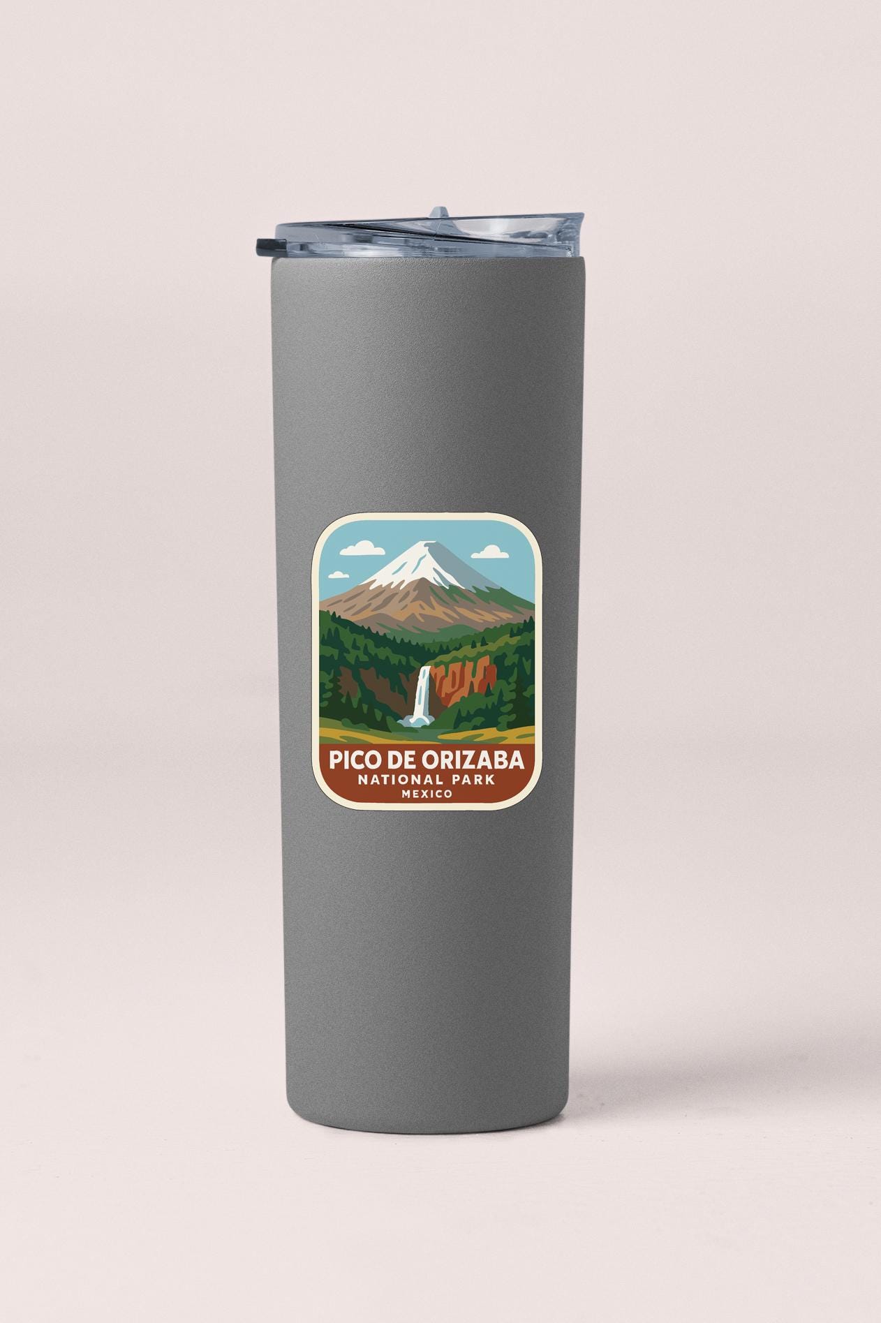 A gray tumbler with a sticker depicting a mountain landscape and a waterfall.