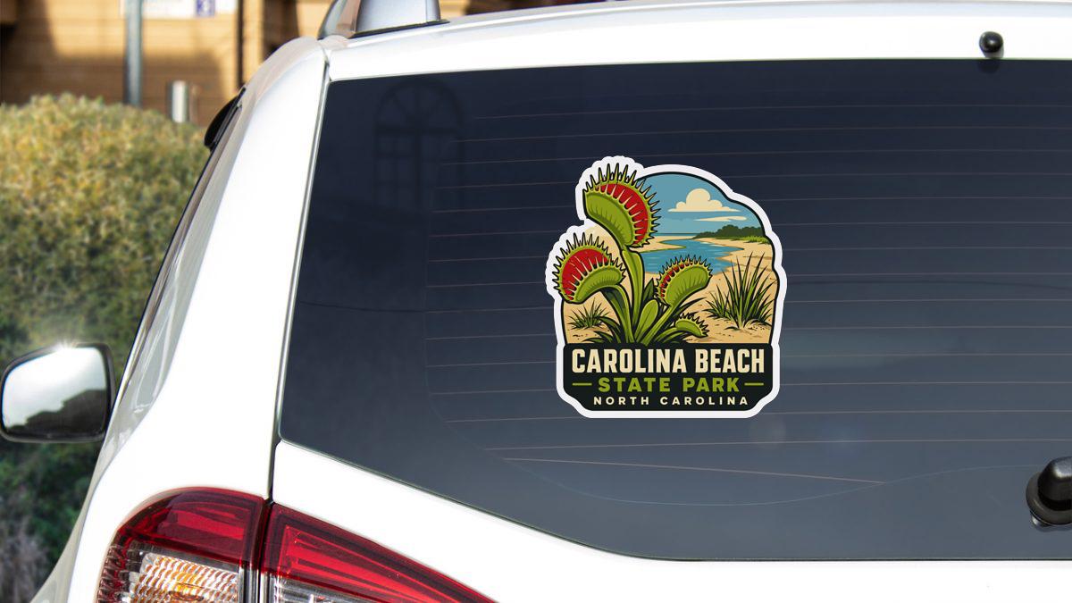 A sticker on the rear window of a white car, depicting a cactus plant and the text "CAROLINA BEACH STATE PARK NORTH CAROLINA".