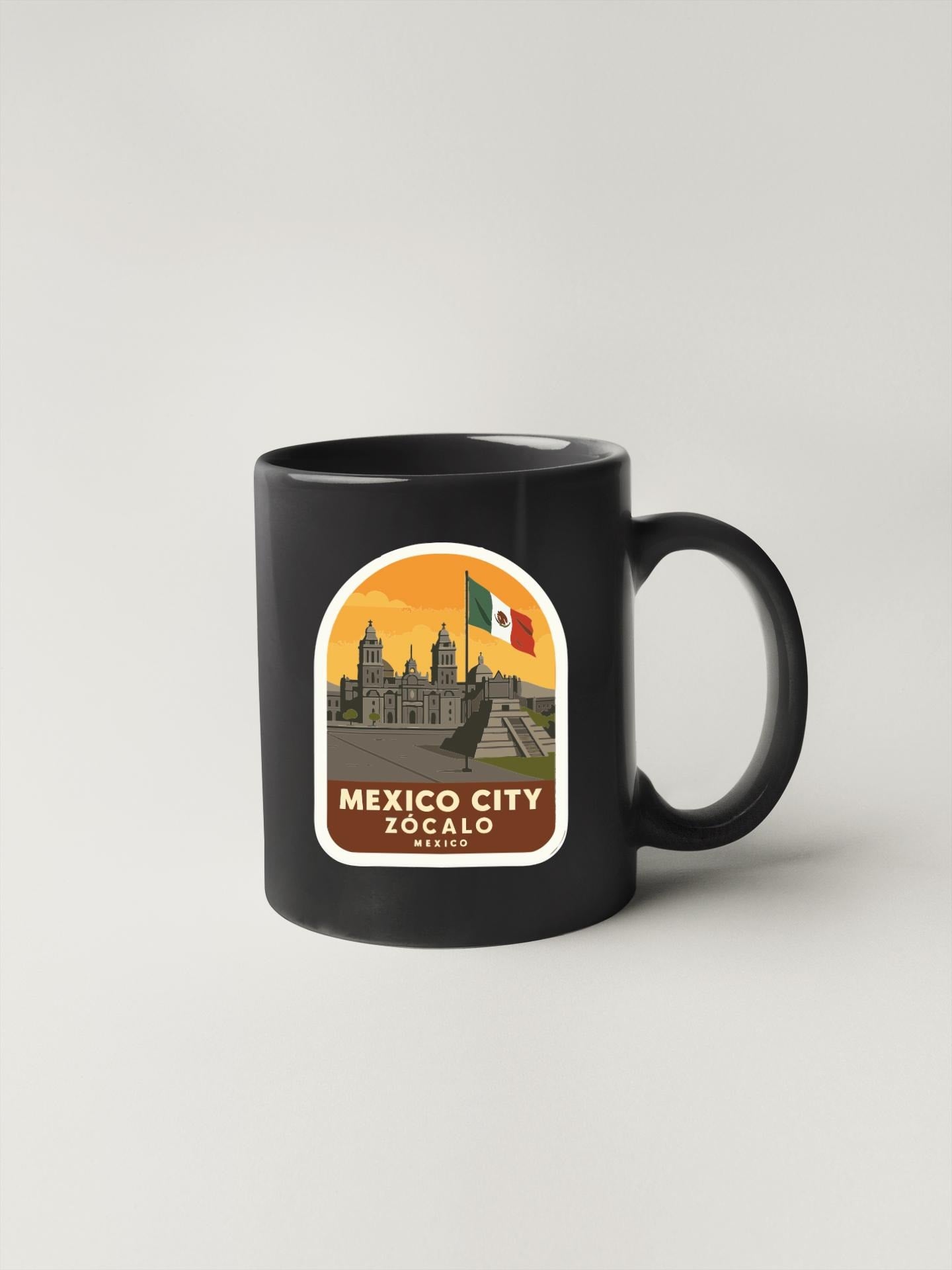 A black coffee mug with a sticker depicting the skyline of Mexico City, specifically the Zocalo district.