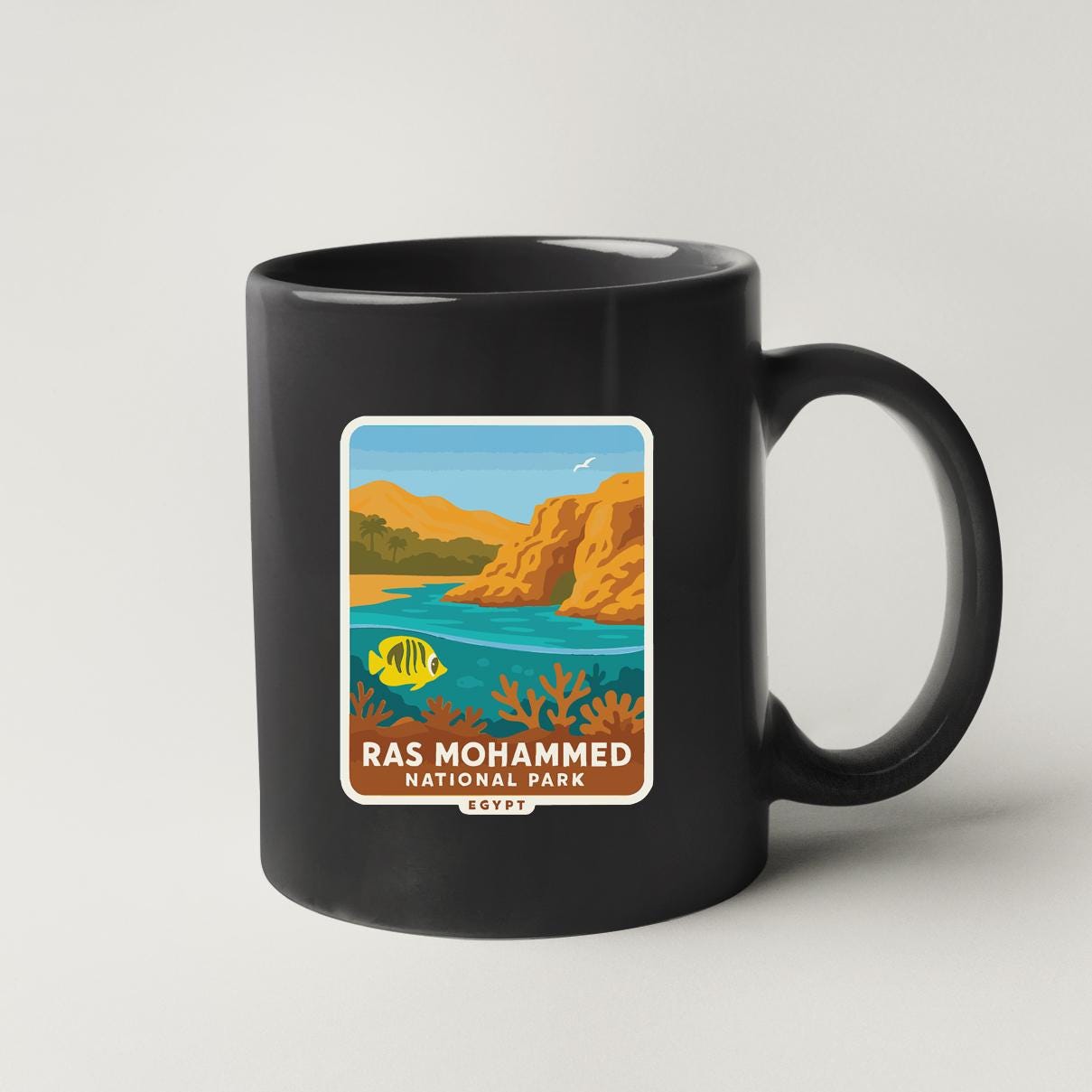 A black coffee mug with a label that features an illustration of Ras Mohammed National Park in Egypt.