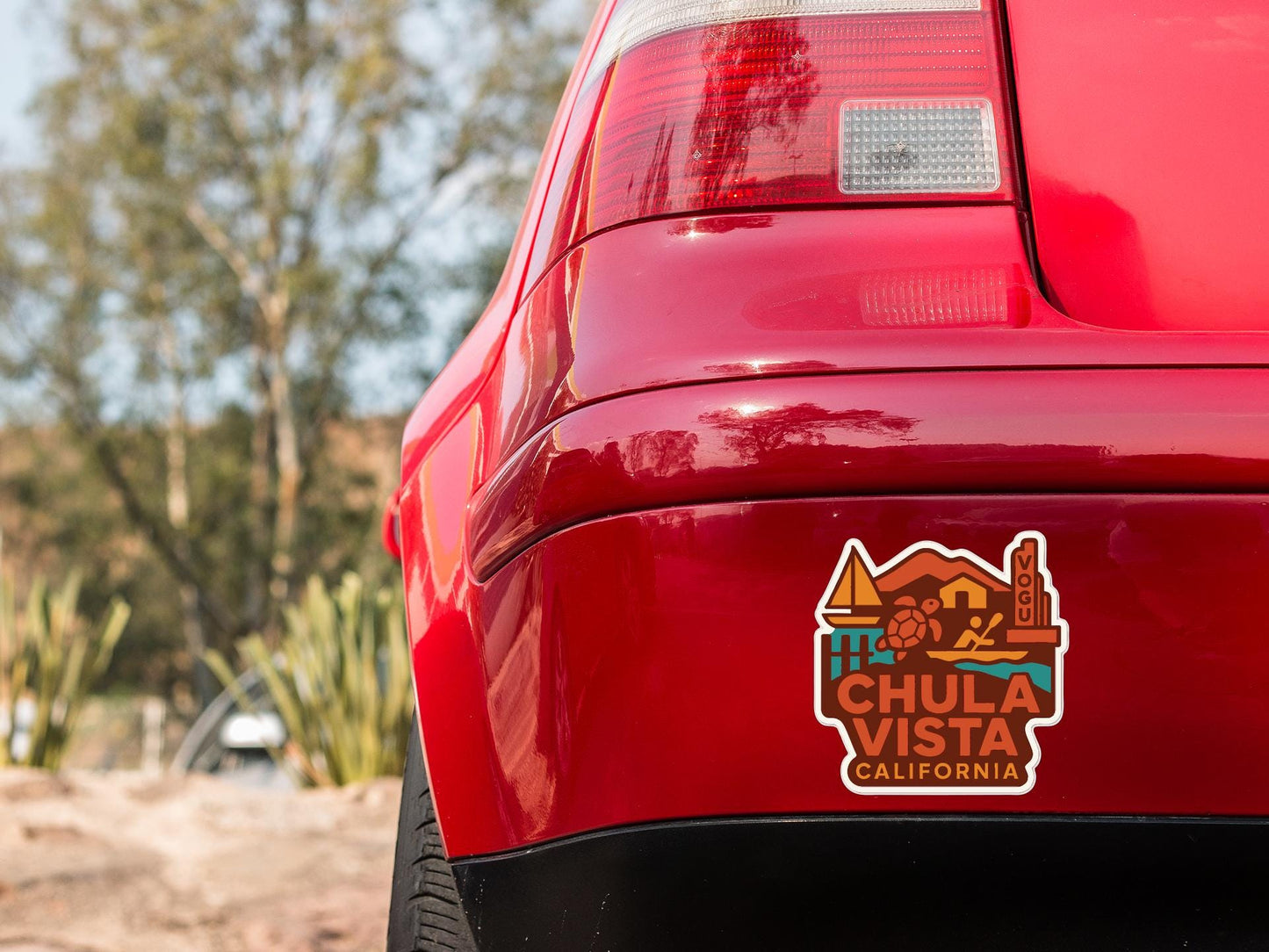the rear end of a red car with a sticker on the trunk that says "CHULA VISTA CALIFORNIA".