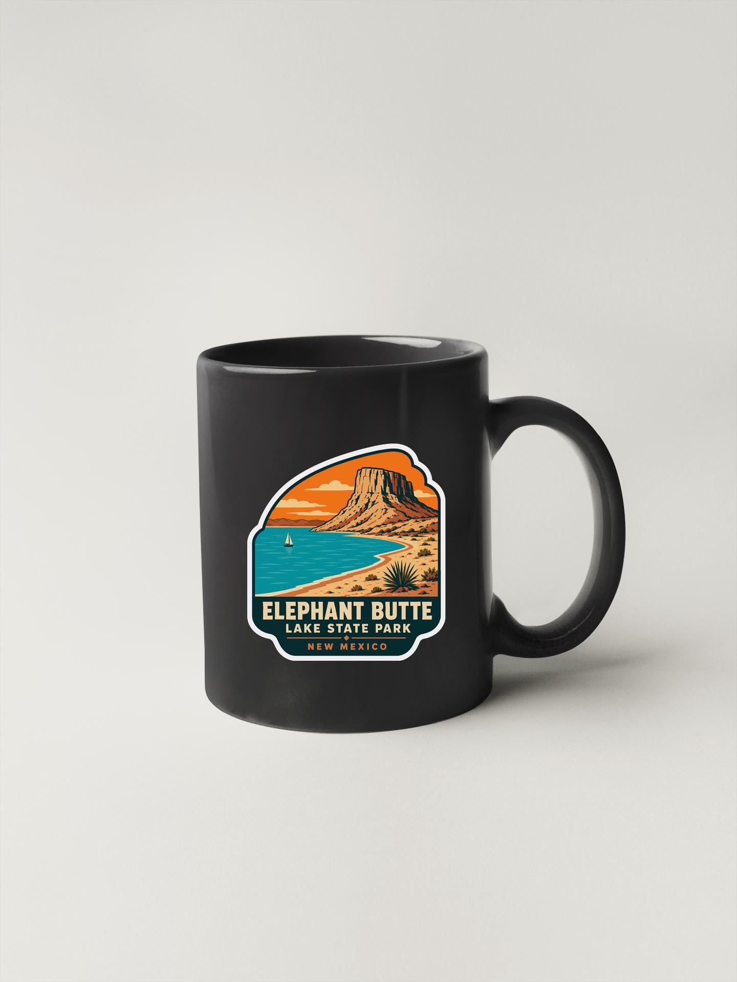 A black coffee mug with a colorful graphic depicting a mountain landscape and a lake.