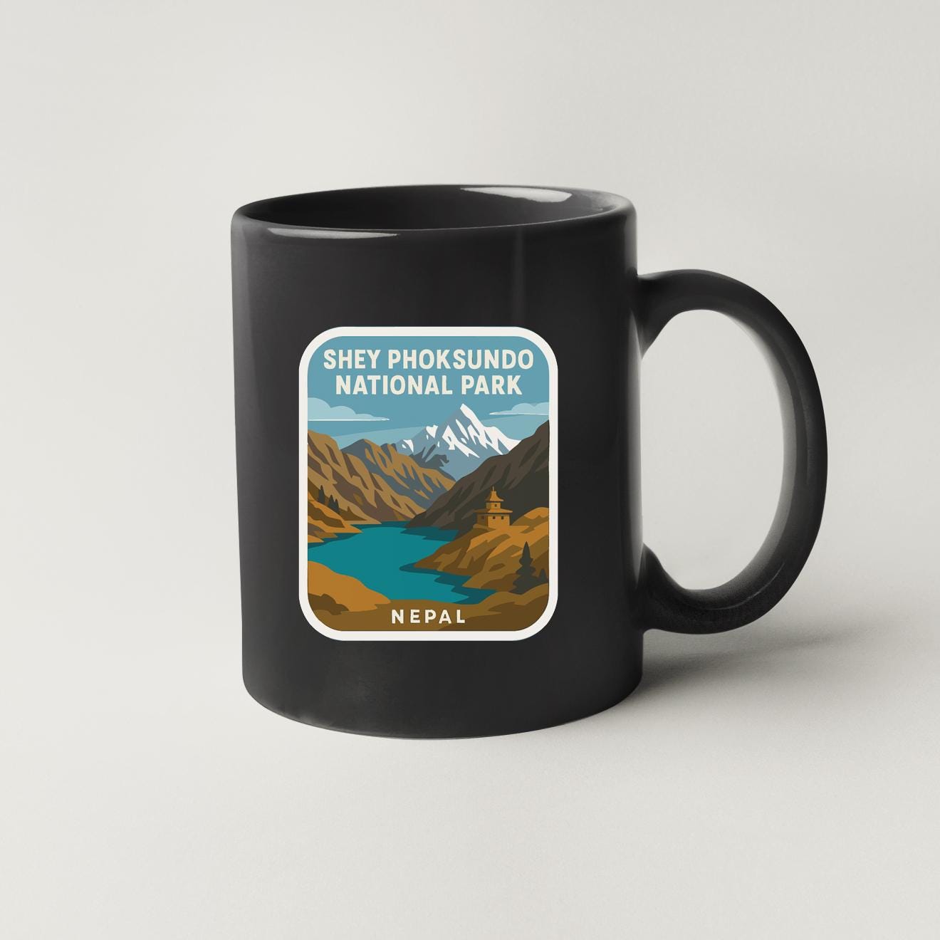 A black coffee mug with a graphic design depicting a scenic mountain landscape with a river and a temple in the background.