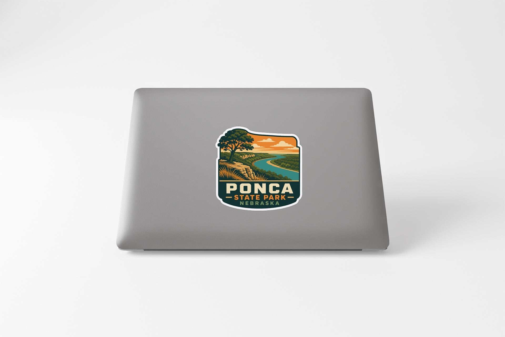 A sticker on the back of a laptop, featuring a scenic landscape with a river and a tree.