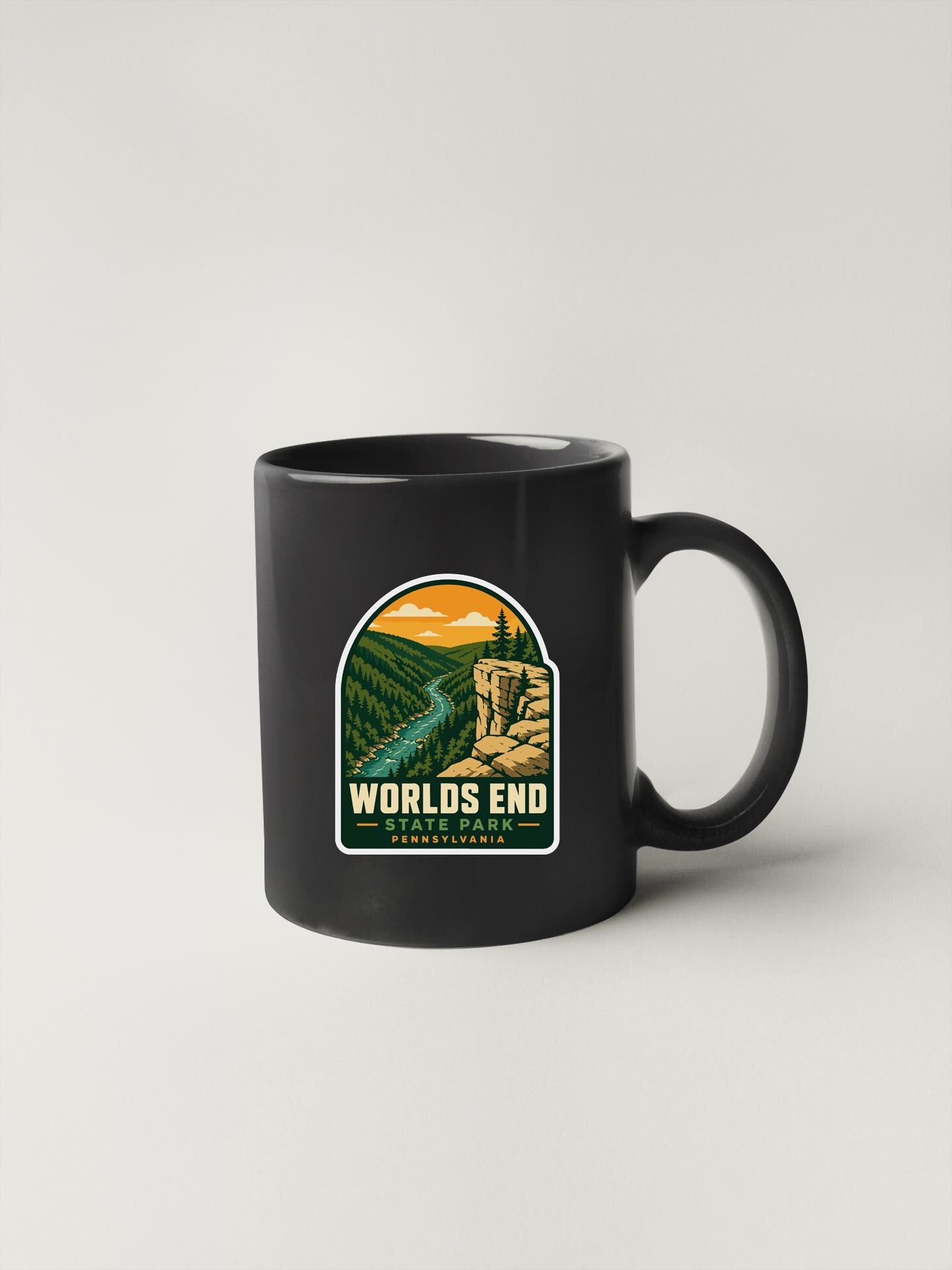 A black coffee mug with a sticker depicting a scenic landscape, including a river, mountains, and a cliff.