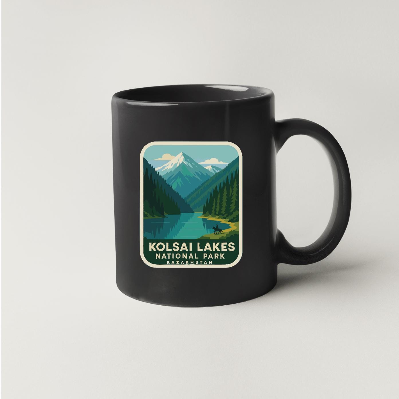 A black coffee mug with a graphic design depicting a scenic mountain landscape with a lake and forest.