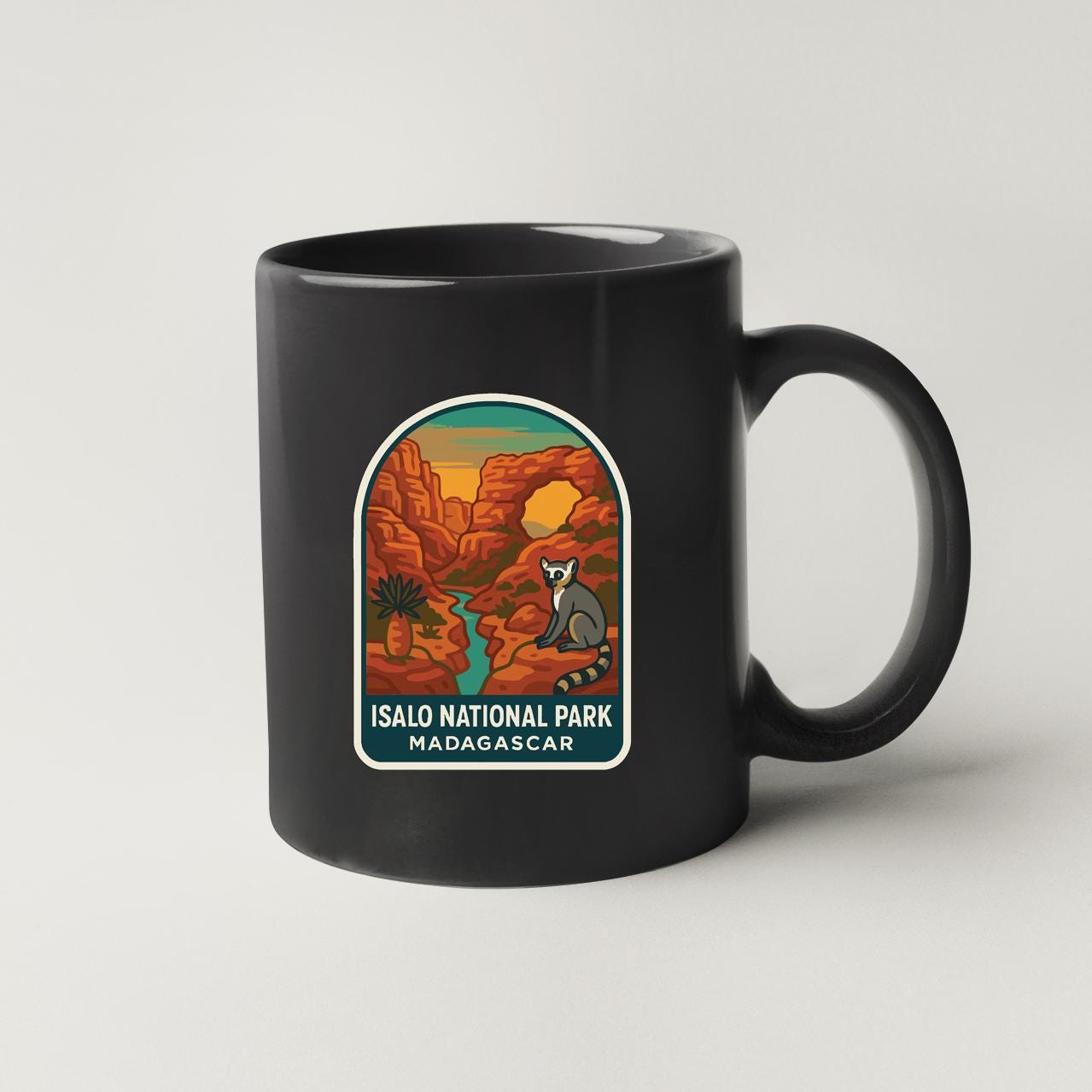 A black coffee mug with a graphic design depicting a scenic landscape of the Isalo National Park in Madagascar.