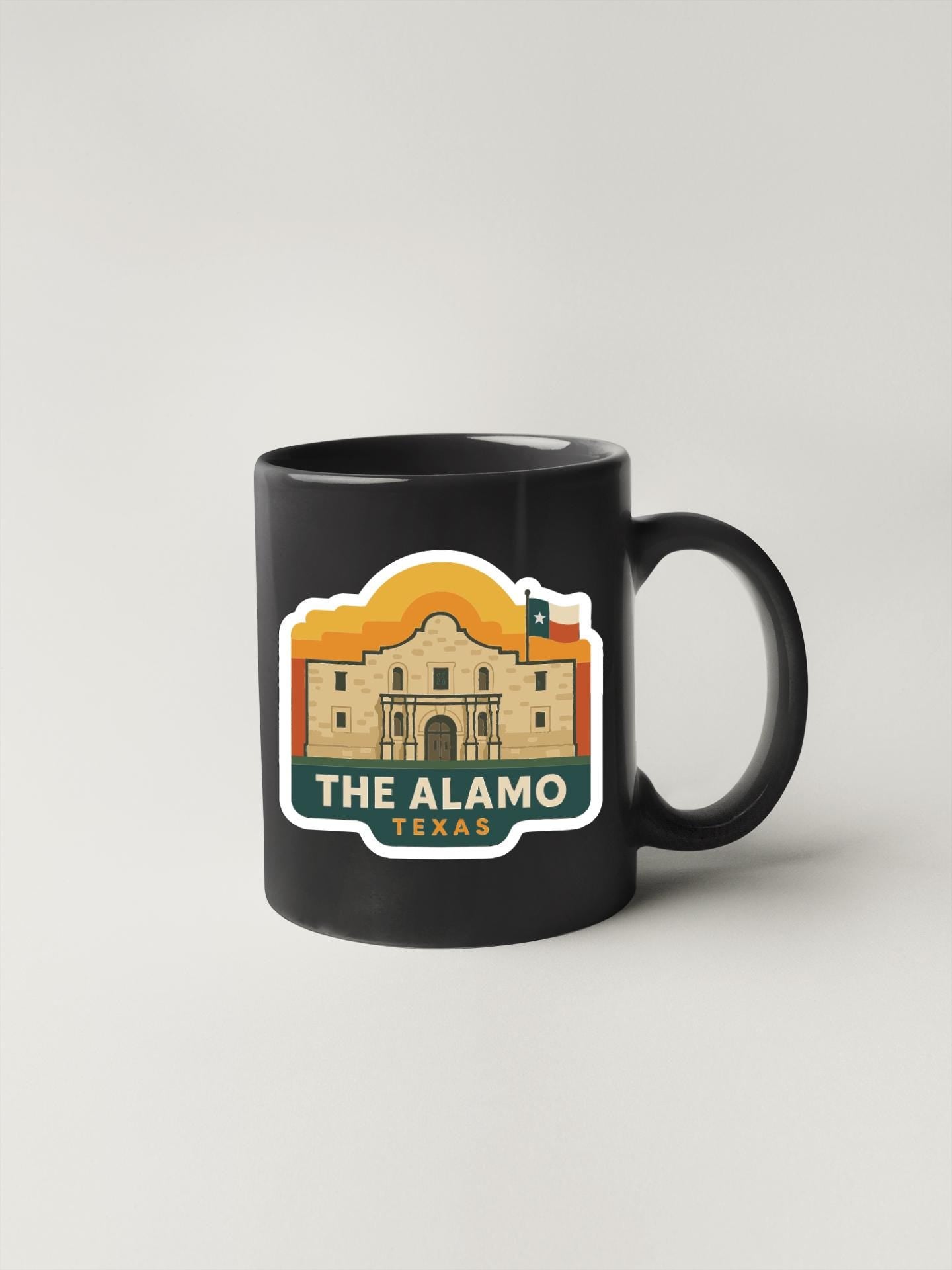 A black coffee mug with a sticker depicting the Alamo, a historic landmark in Texas.