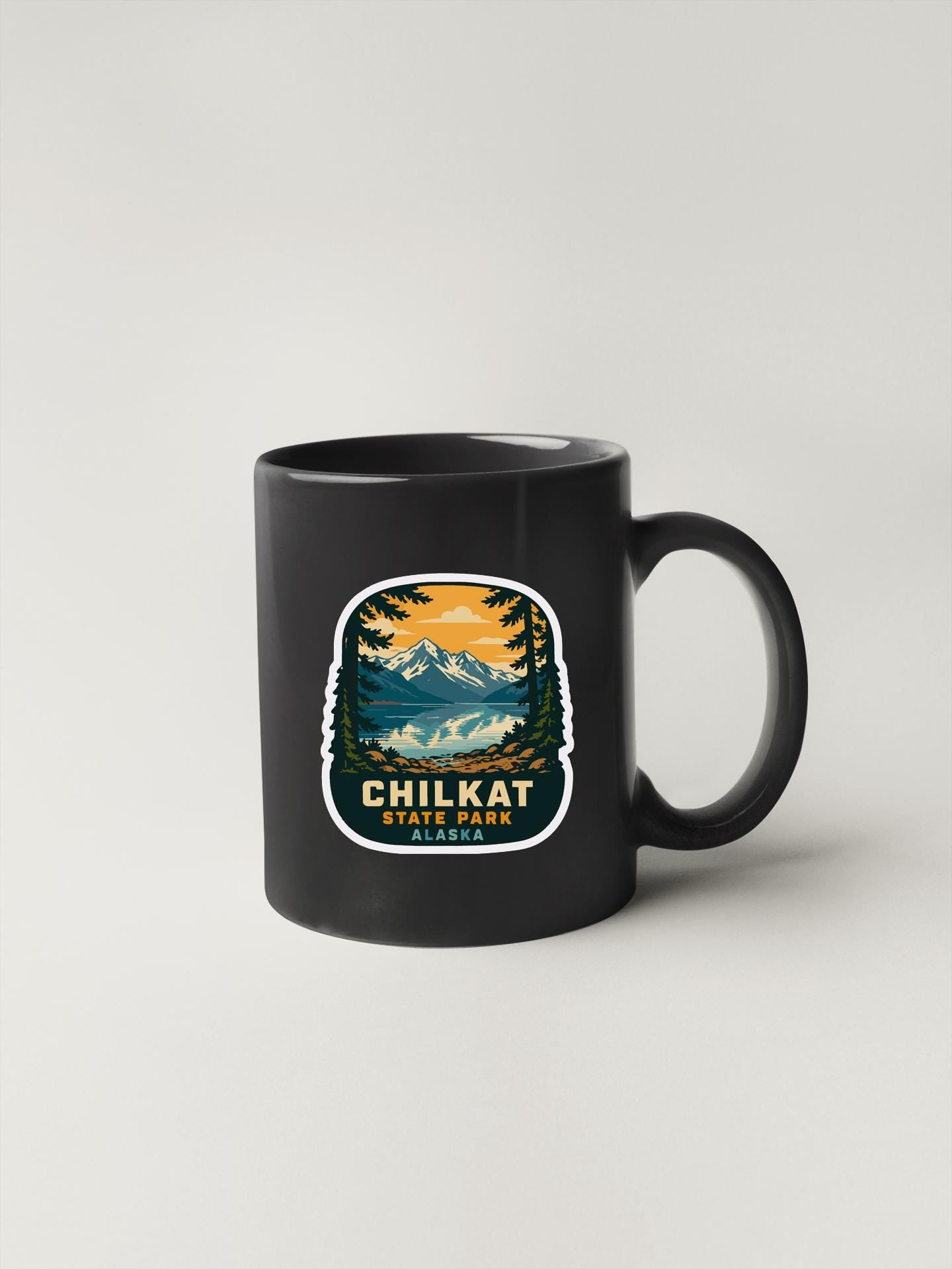 A black coffee mug with a sticker depicting a scenic mountain landscape.