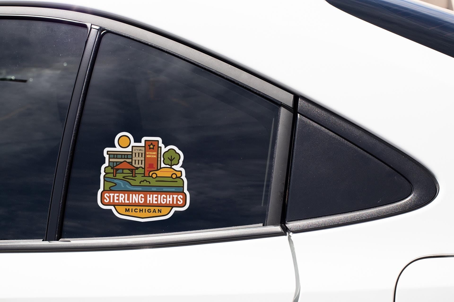 A car window sticker with a colorful illustration of a cityscape and the text "Sterling Heights, Michigan".