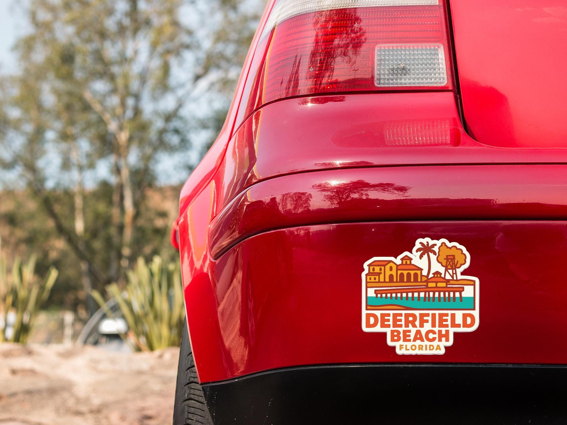 the rear end of a red car with a sticker on the back window that says "Deerfield Beach, Florida".