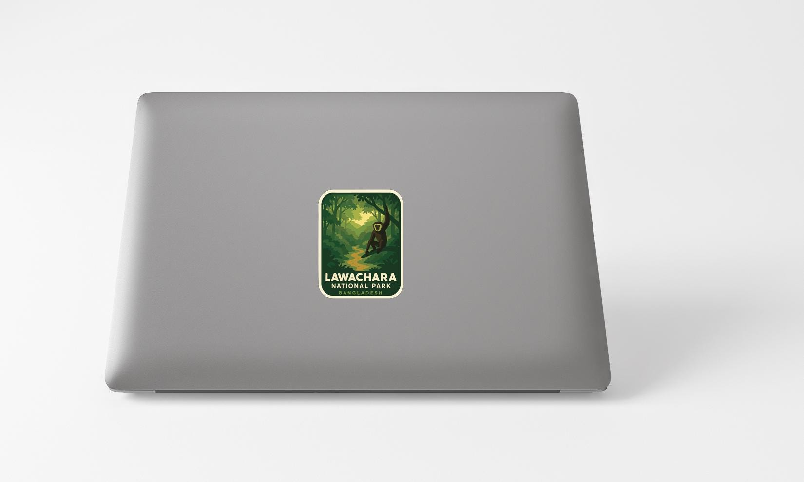 A sticker with a forest scene and text on a grey laptop.