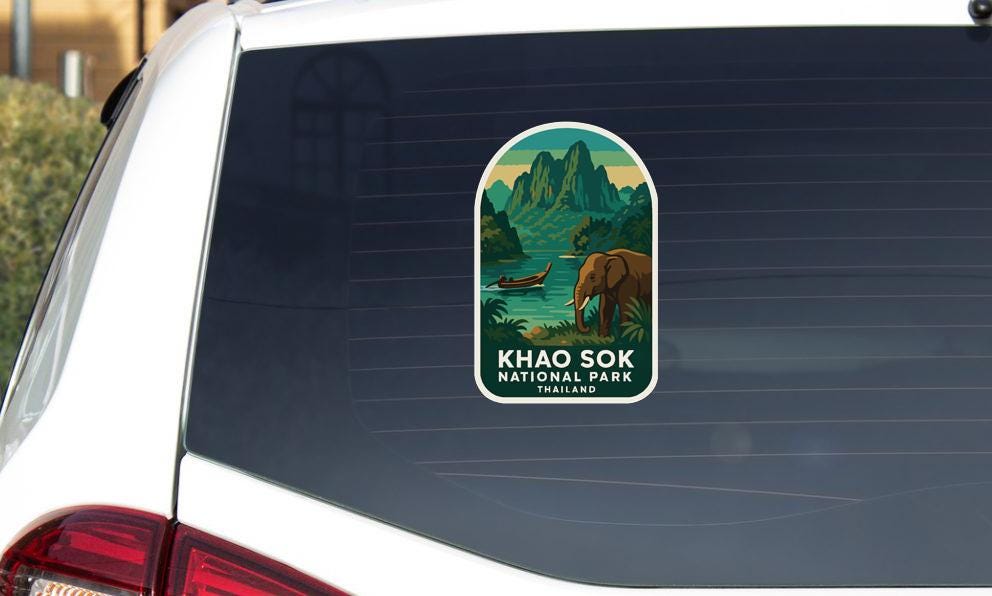 A sticker on the rear window of a car, depicting a scenic landscape with mountains, a river, and an elephant.
