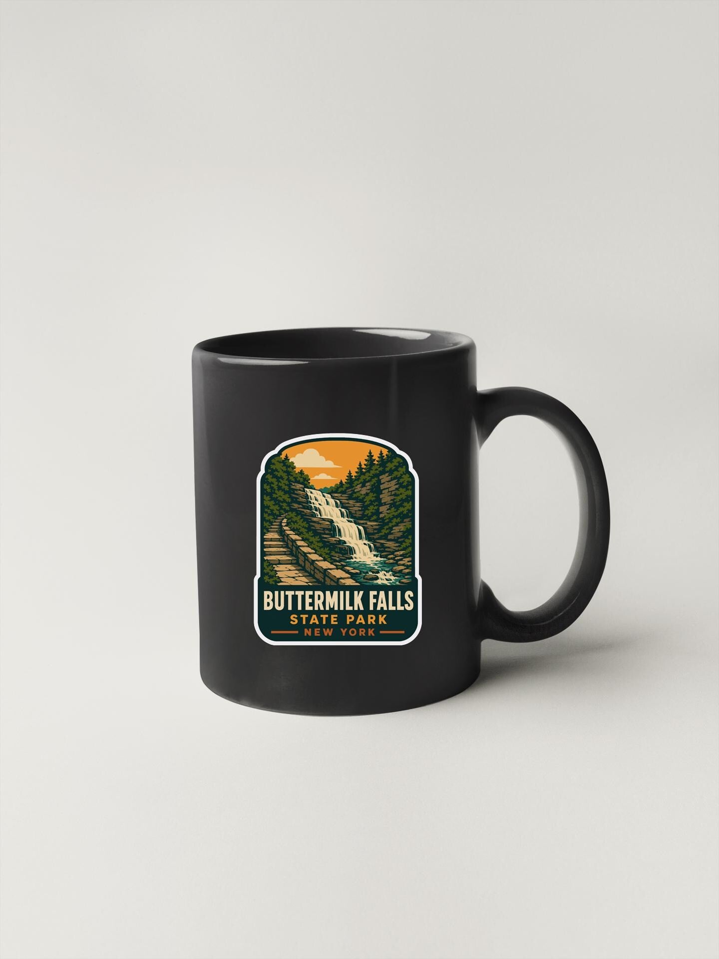 A black coffee mug with a graphic design depicting Buttermilk Falls State Park in New York.