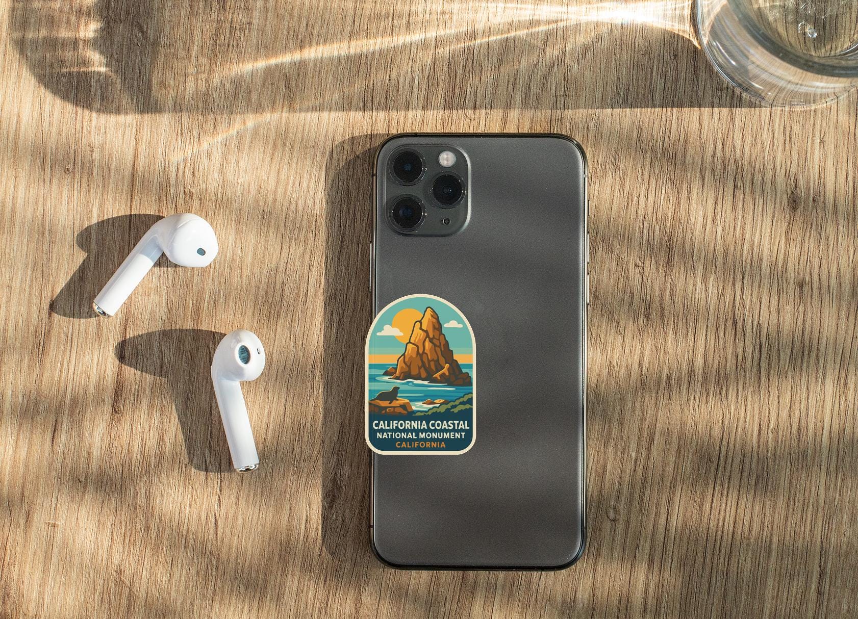 a smartphone with a sticker on the back, placed on a wooden surface alongside a pair of white earbuds.