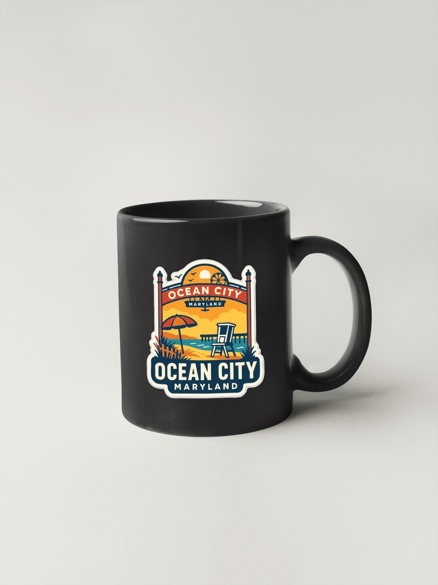 A black coffee mug with a colorful graphic design depicting a beach scene and the text "OCEAN CITY, MARYLAND" printed on it.