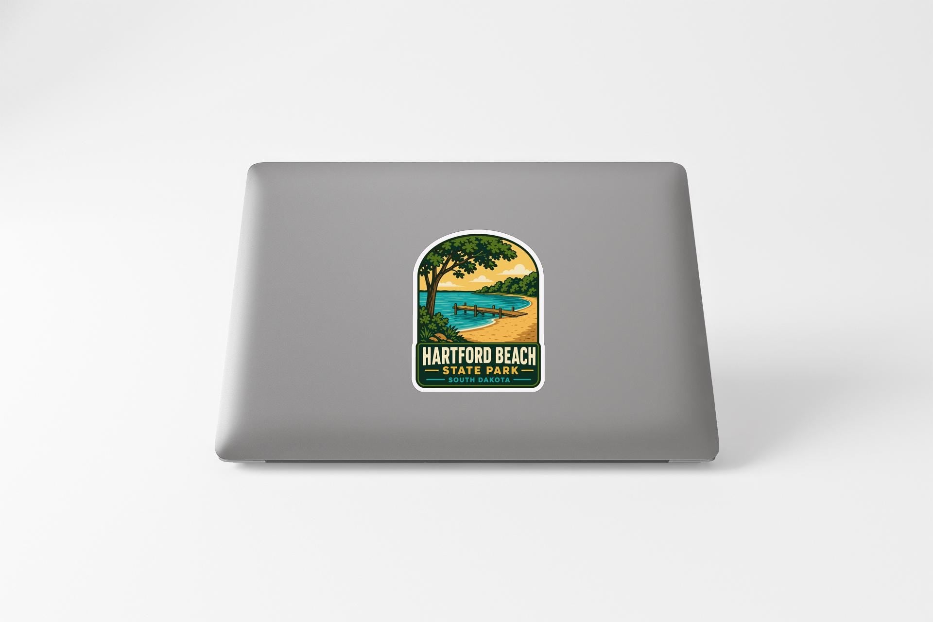 A sticker on the back of a laptop, depicting a scenic landscape with a beach, trees, and a body of water.