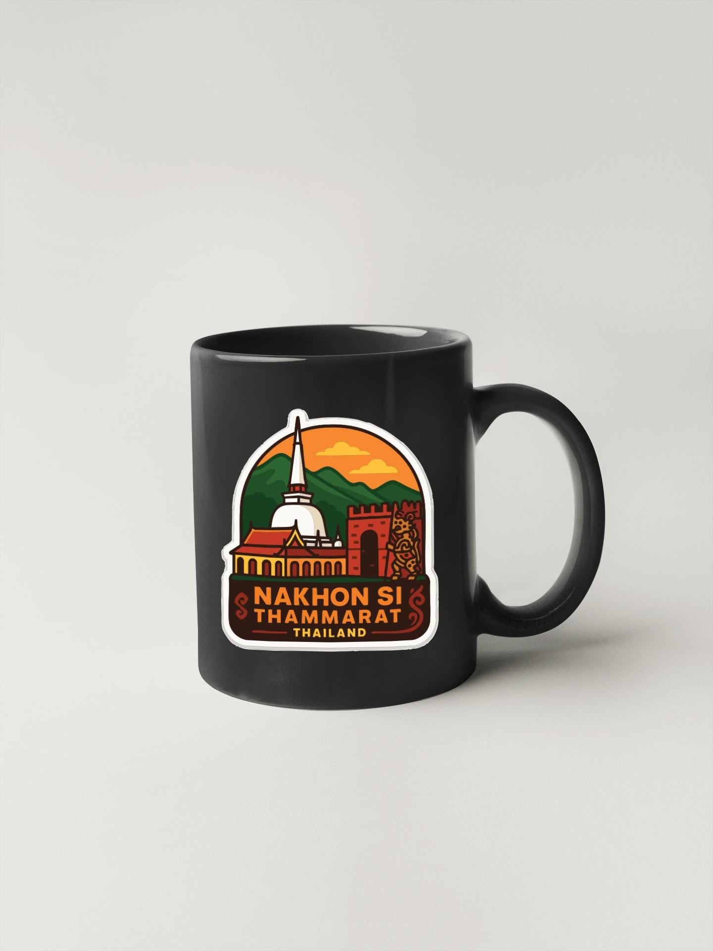 A black coffee mug with a colorful graphic design depicting a temple and mountains, along with the text "Nakhon Si Thammarat Thailand".