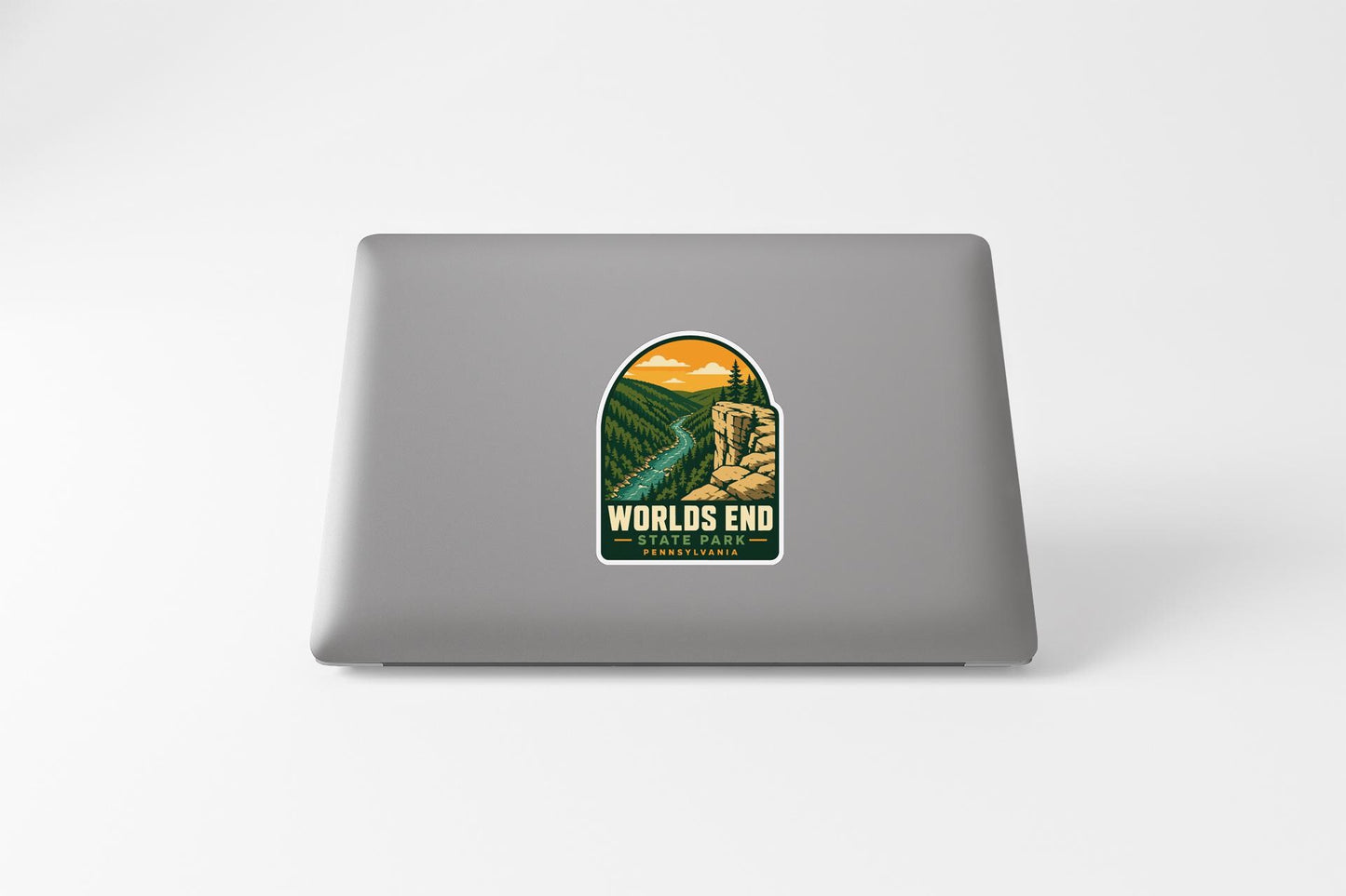A sticker on the back of a laptop, depicting a scenic landscape with mountains, trees, and a winding river.