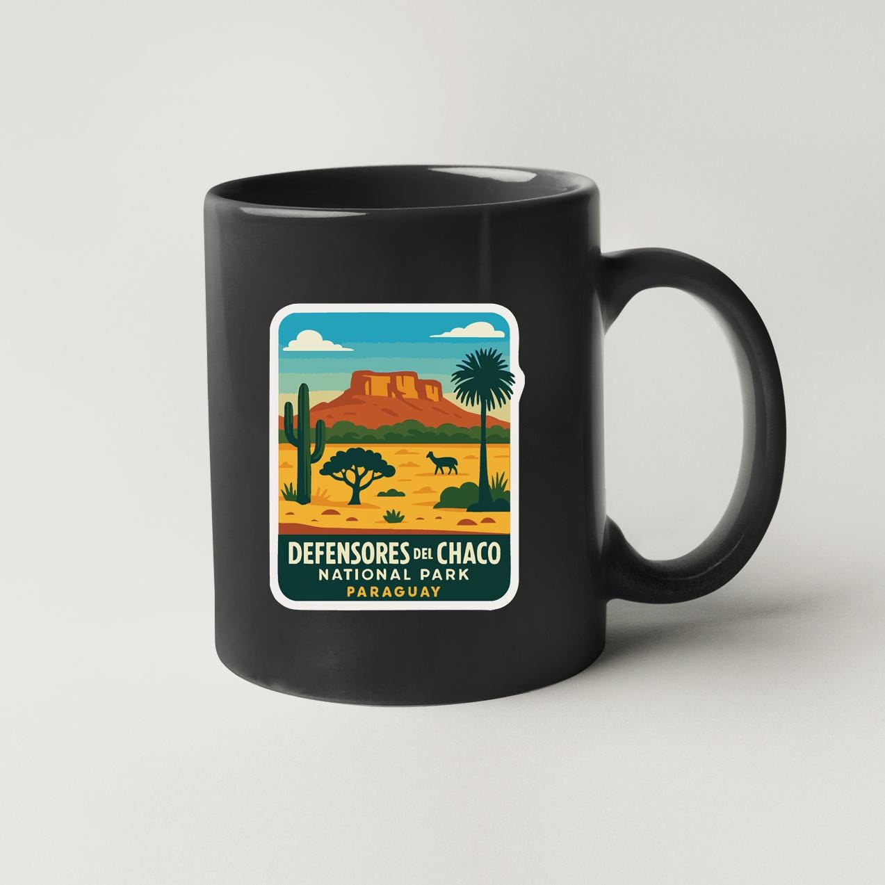A black coffee mug with a graphic design depicting a desert landscape with mountains, cacti, and a palm tree.