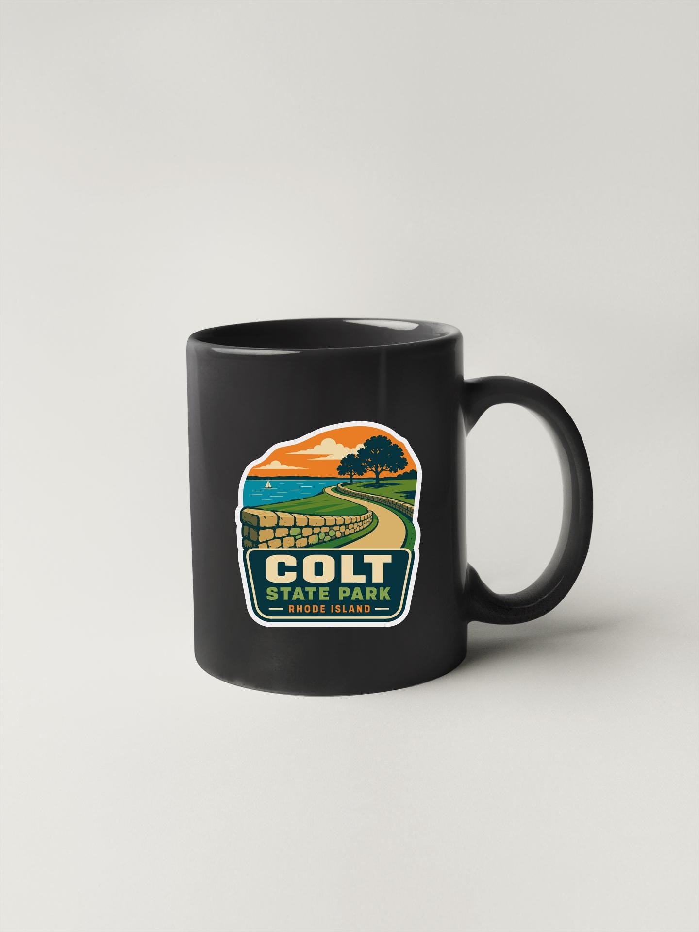 A black coffee mug with a graphic design depicting a scenic landscape, including a road, trees, and a body of water.