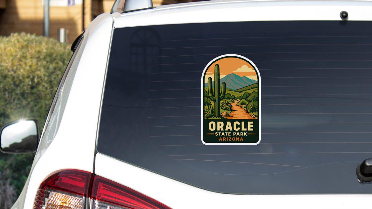 A sticker on the rear window of a white car, depicting a desert landscape with mountains in the background.