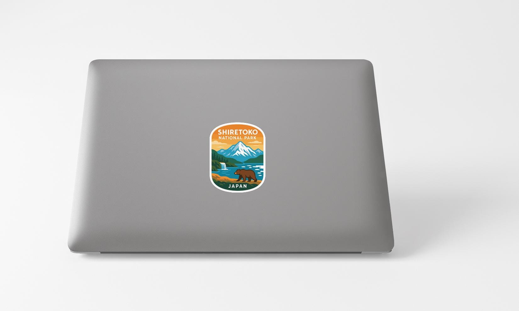 A sticker on the back of a laptop, depicting a scenic landscape with a mountain, a bear, and a body of water.