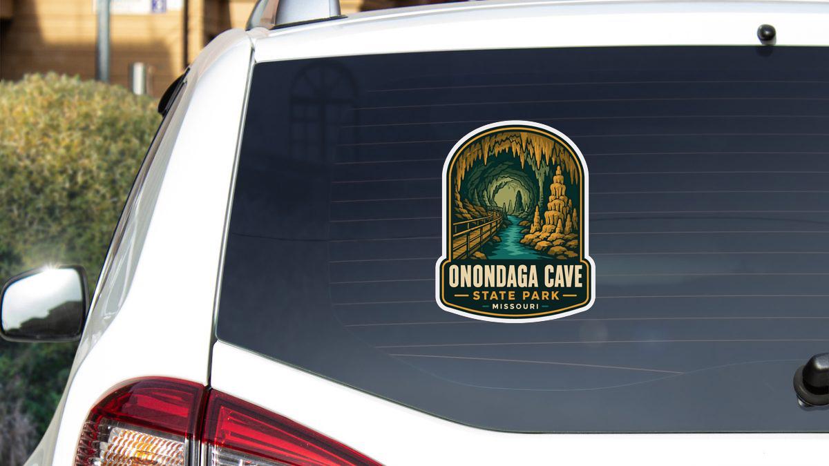 A sticker on the rear window of a white car, depicting the Onondaga Cave State Park in Missouri.