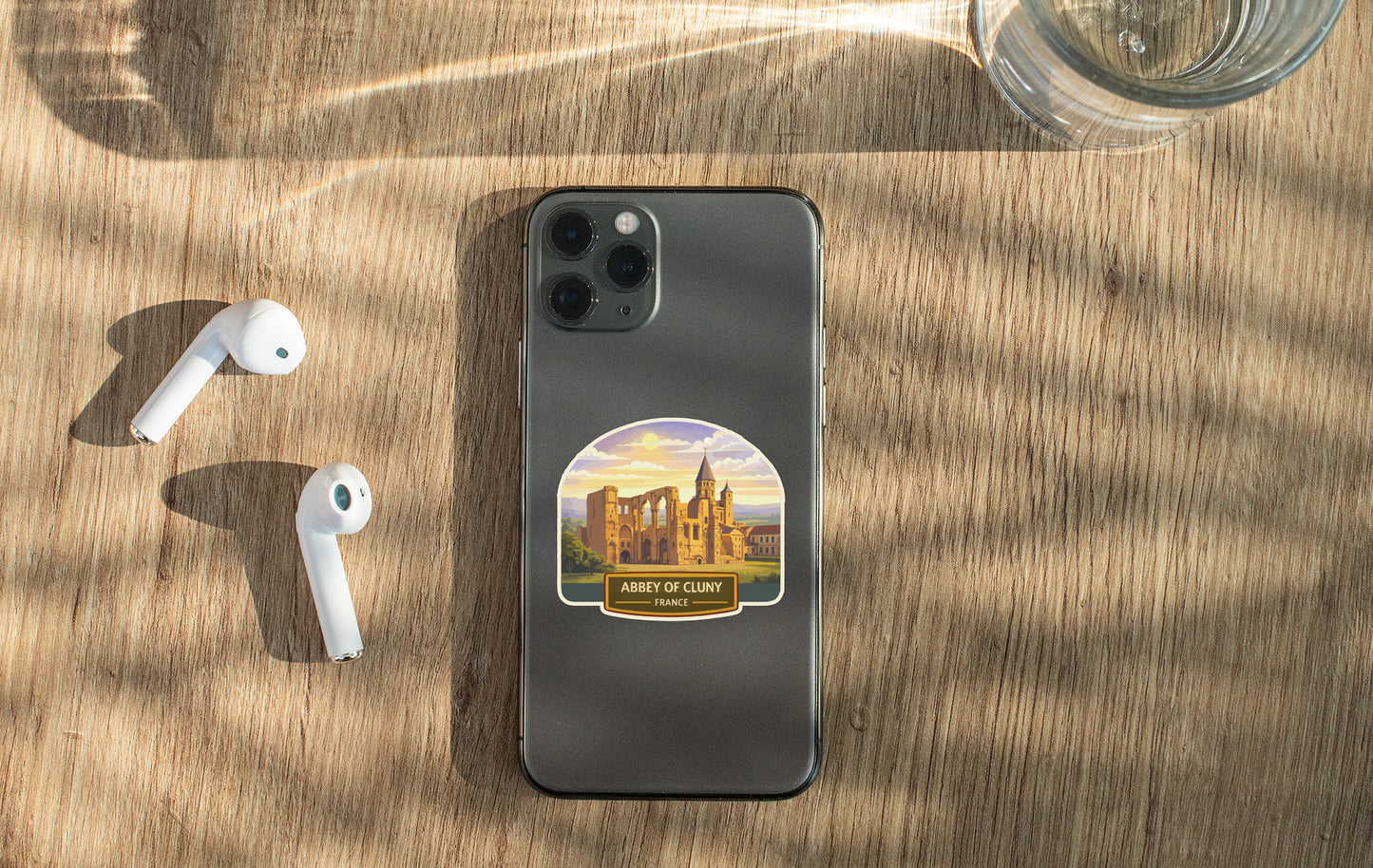 a smartphone with a sticker of a castle on it, placed on a wooden surface alongside a pair of white earbuds and a glass of water.