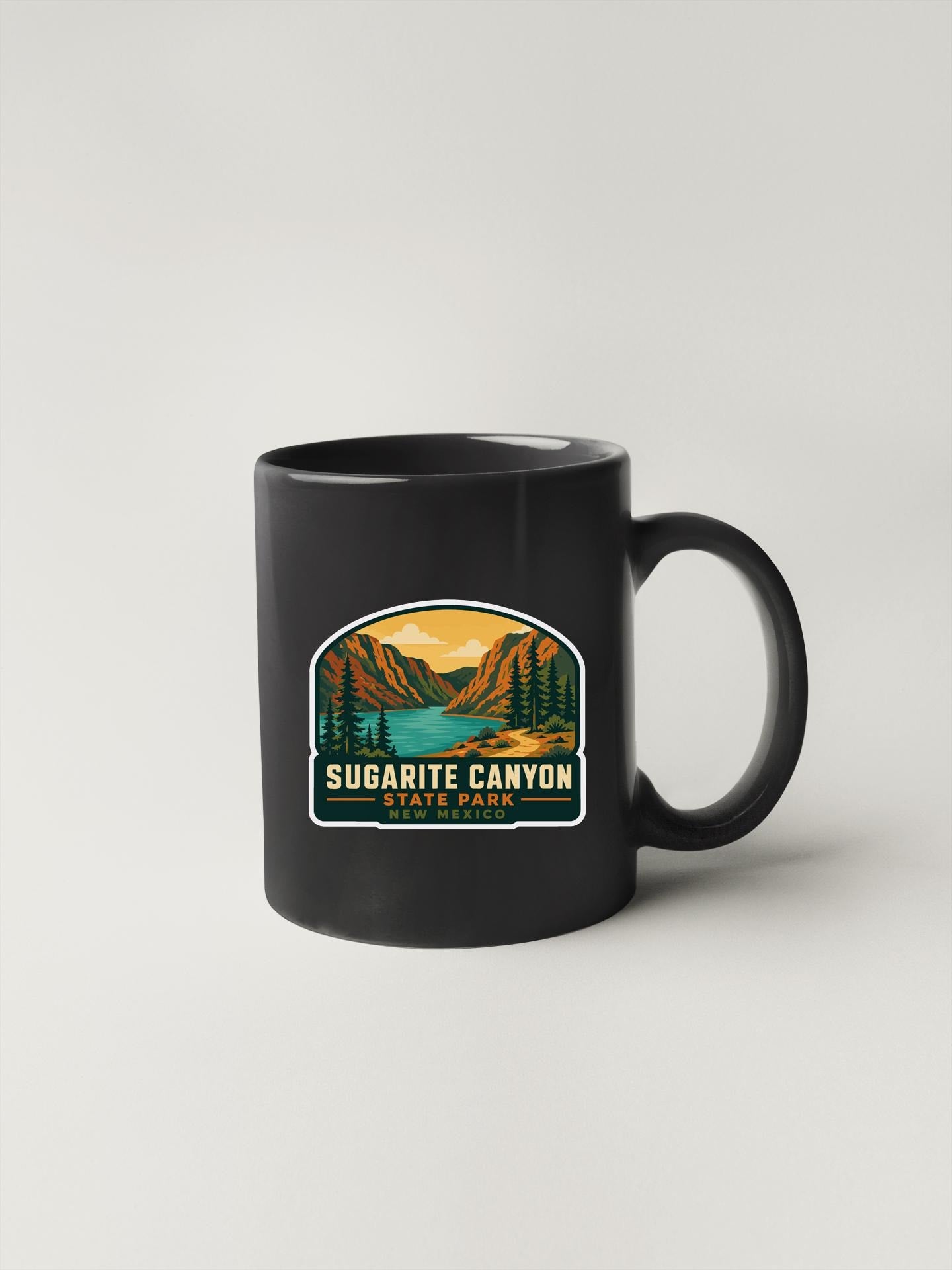 A black coffee mug with a graphic design depicting Sugarite Canyon, a scenic landscape with mountains, trees, and a lake.