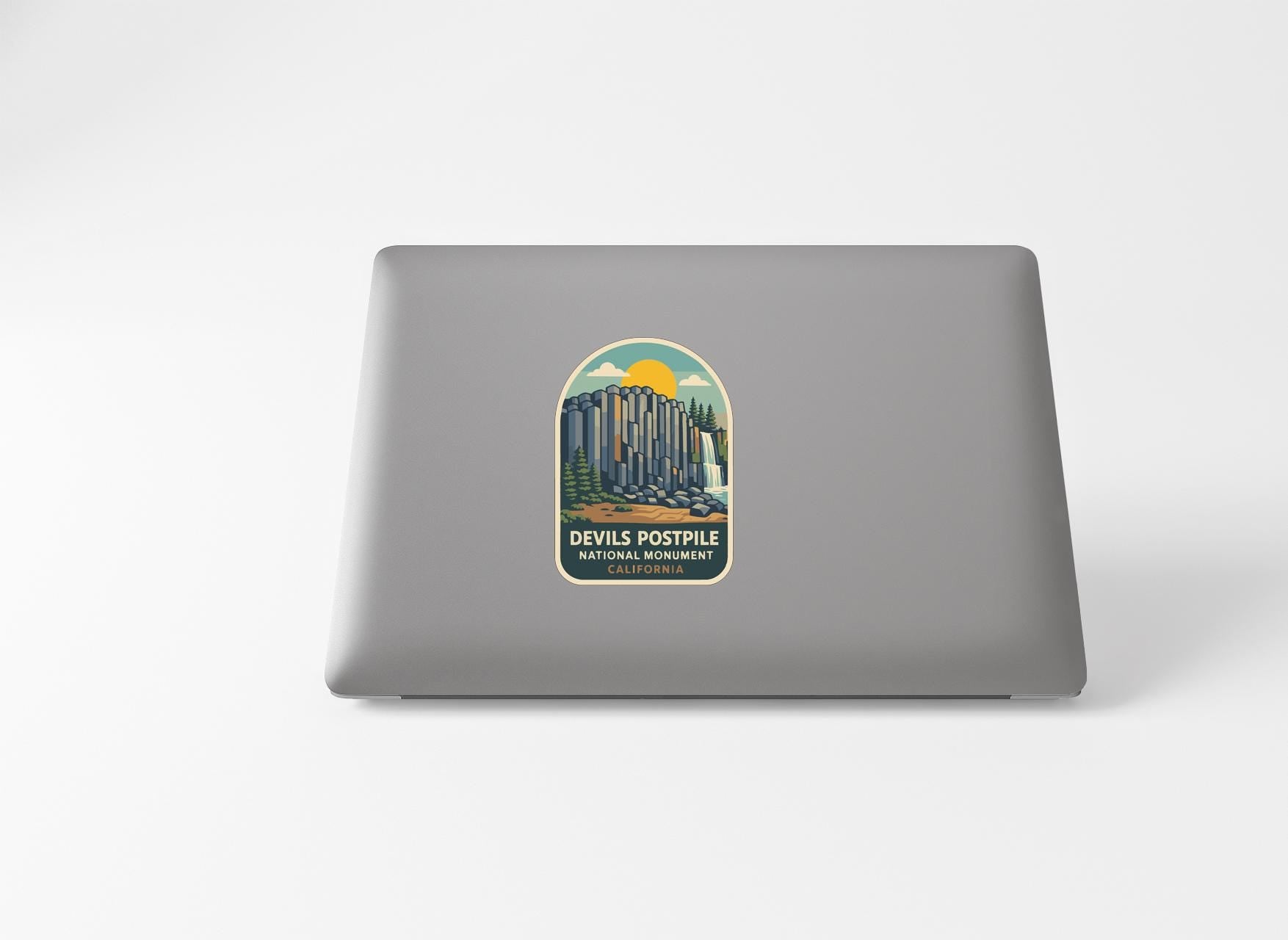 A sticker on the back of a laptop, depicting a mountain landscape with a sun and clouds.