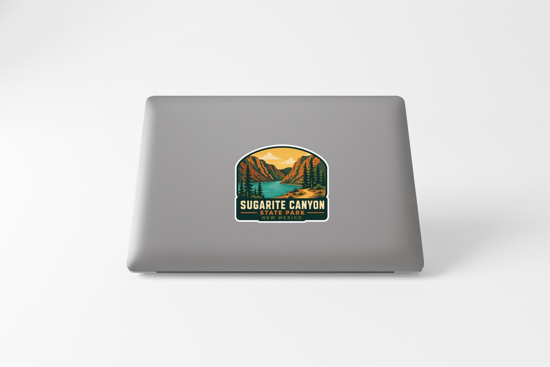 A sticker on the back of a laptop that features a scenic landscape with mountains, trees, and a lake, along with the text "SUGARITE CANYON STATE PARK".