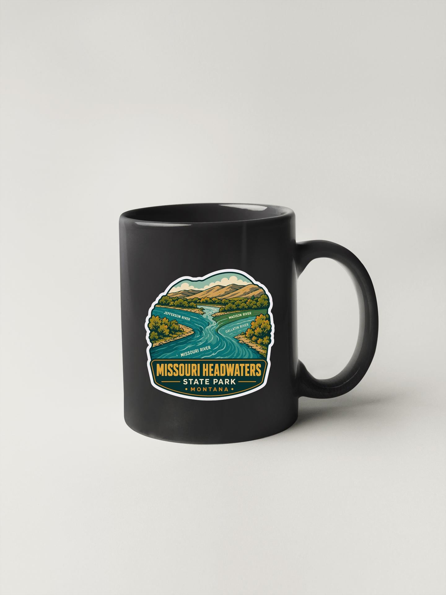 A black coffee mug with a graphic design depicting a scenic landscape featuring a river and mountains.