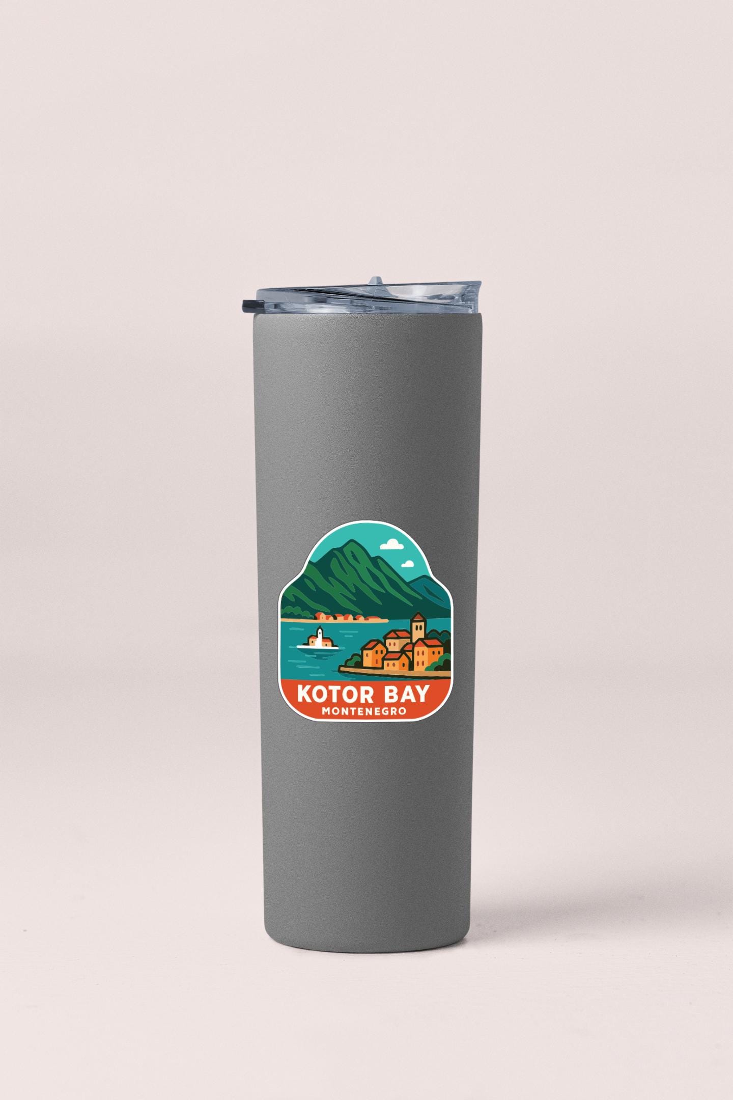 A gray insulated tumbler with a sticker depicting a scenic mountain landscape and a small town.