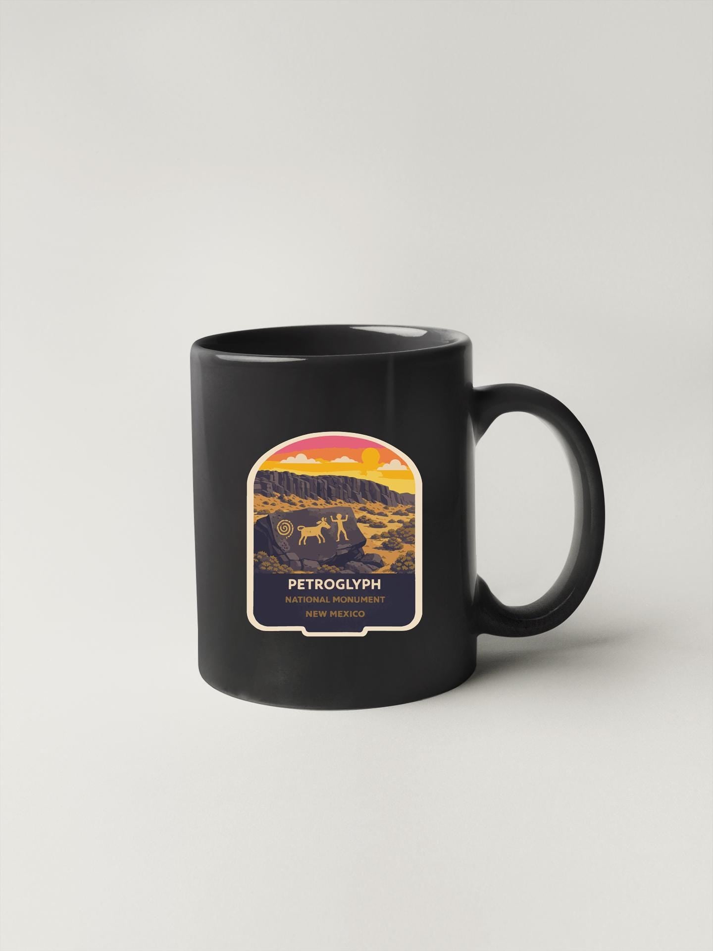 A black coffee mug with a graphic design depicting a desert landscape with mountains and a sunset.