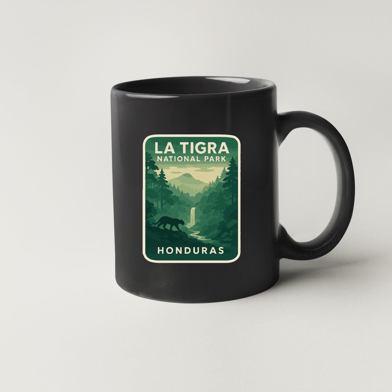 A black coffee mug with a sticker depicting a forest scene and a waterfall, along with the text "LA TIGRA NATIONAL PARK HONDURAS".